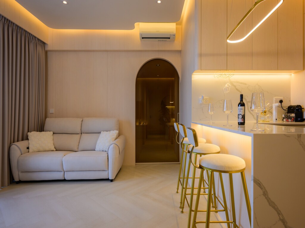 Modern living room with beige sofa, gold bar stools, marble counter, and dim warm lighting.