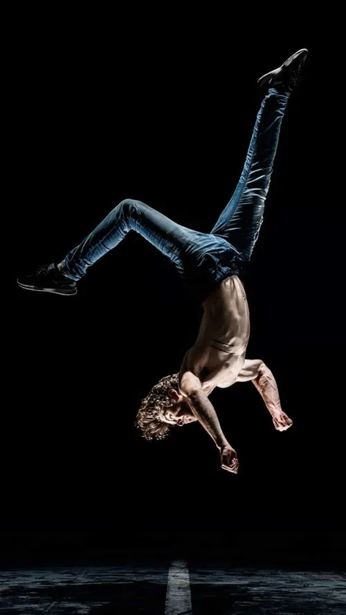 Junger Mann macht eine akrobatische Handstandbewegung in einer dunklen Umgebung.