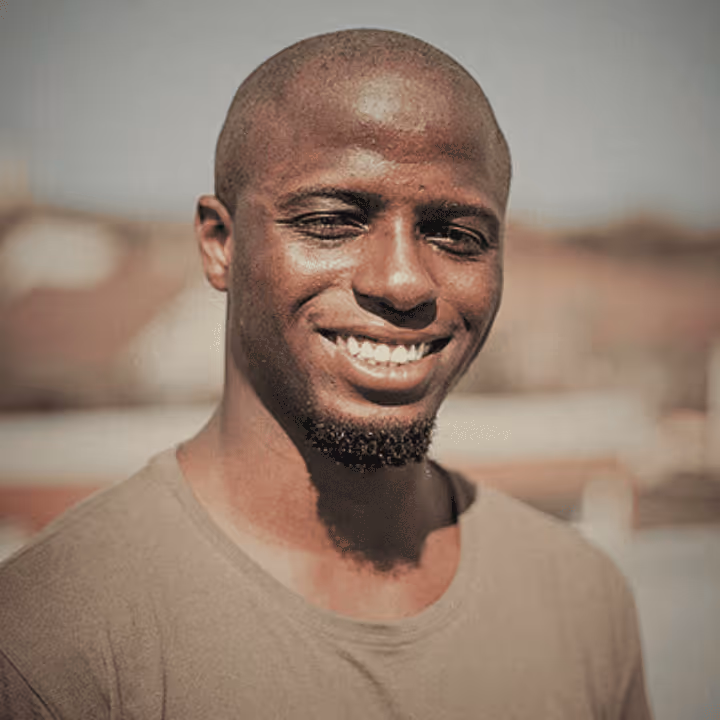 Lächelnder junger Mann mit kurzem Bart und kahlem Kopf im Freien.