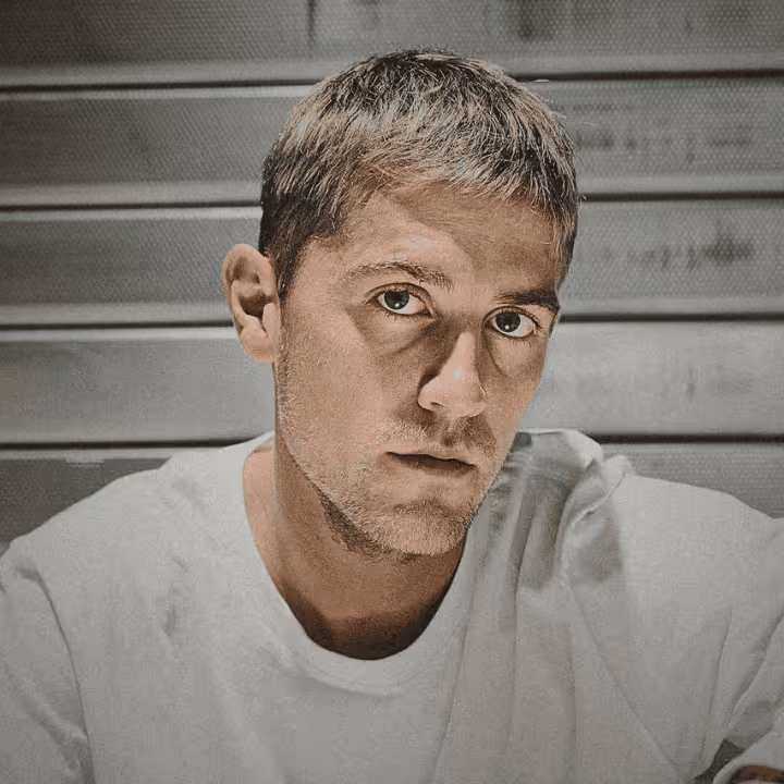 Porträt eines jungen Mannes mit kurzem Haar und weißem T-Shirt vor einem grauen Hintergrund mit horizontalen Linien.