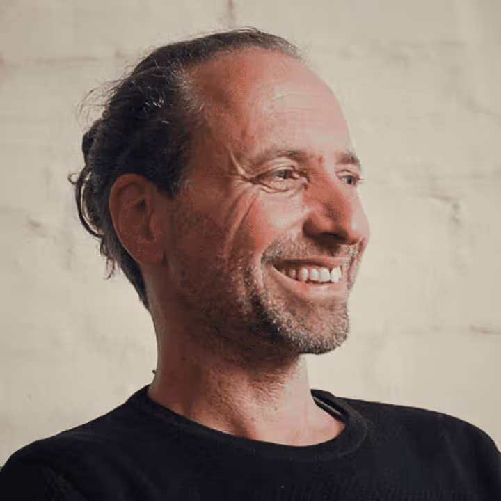 Porträt eines lächelnden Mannes mit zusammengebundenen Haaren und Bart, der nach rechts schaut.