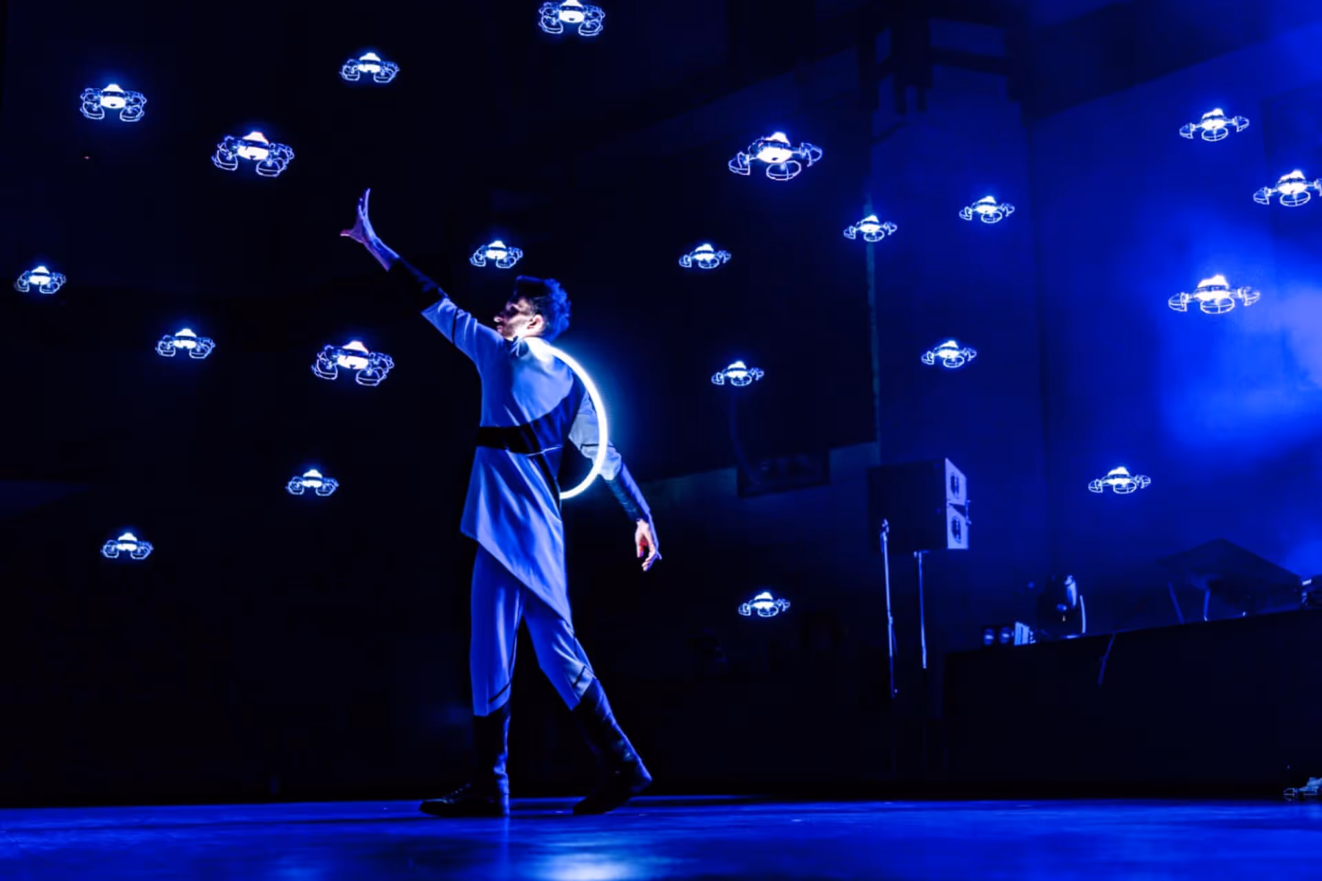 Tänzer auf einer Bühne mit blauen Drohneneffekten, die in der Luft schweben.