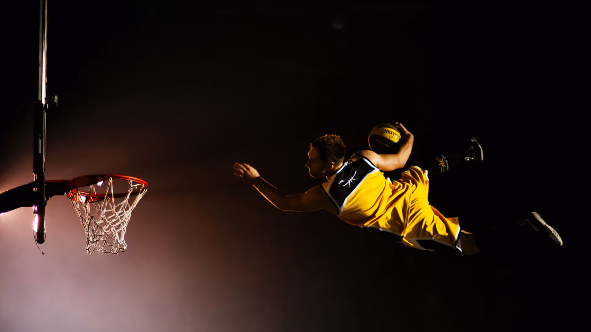 Basketballspieler in gelber Uniform springt in der Luft zum Korb zum Dunking mit Ball in der rechten Hand.