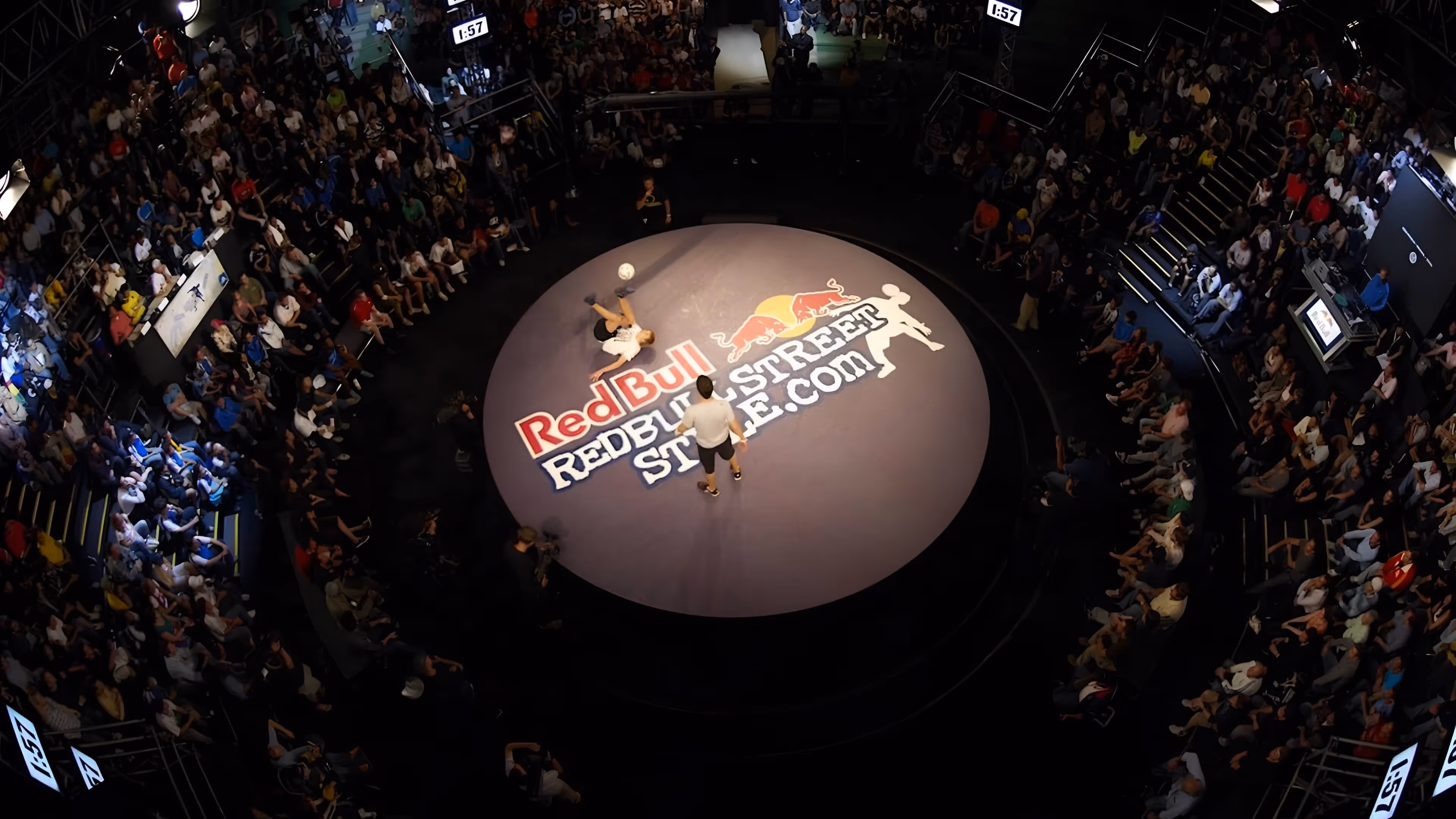 Zuschauer umringen eine runde Bühne mit Red Bull Street Style-Logo, auf der zwei Männer Fußballtricks vorführen.