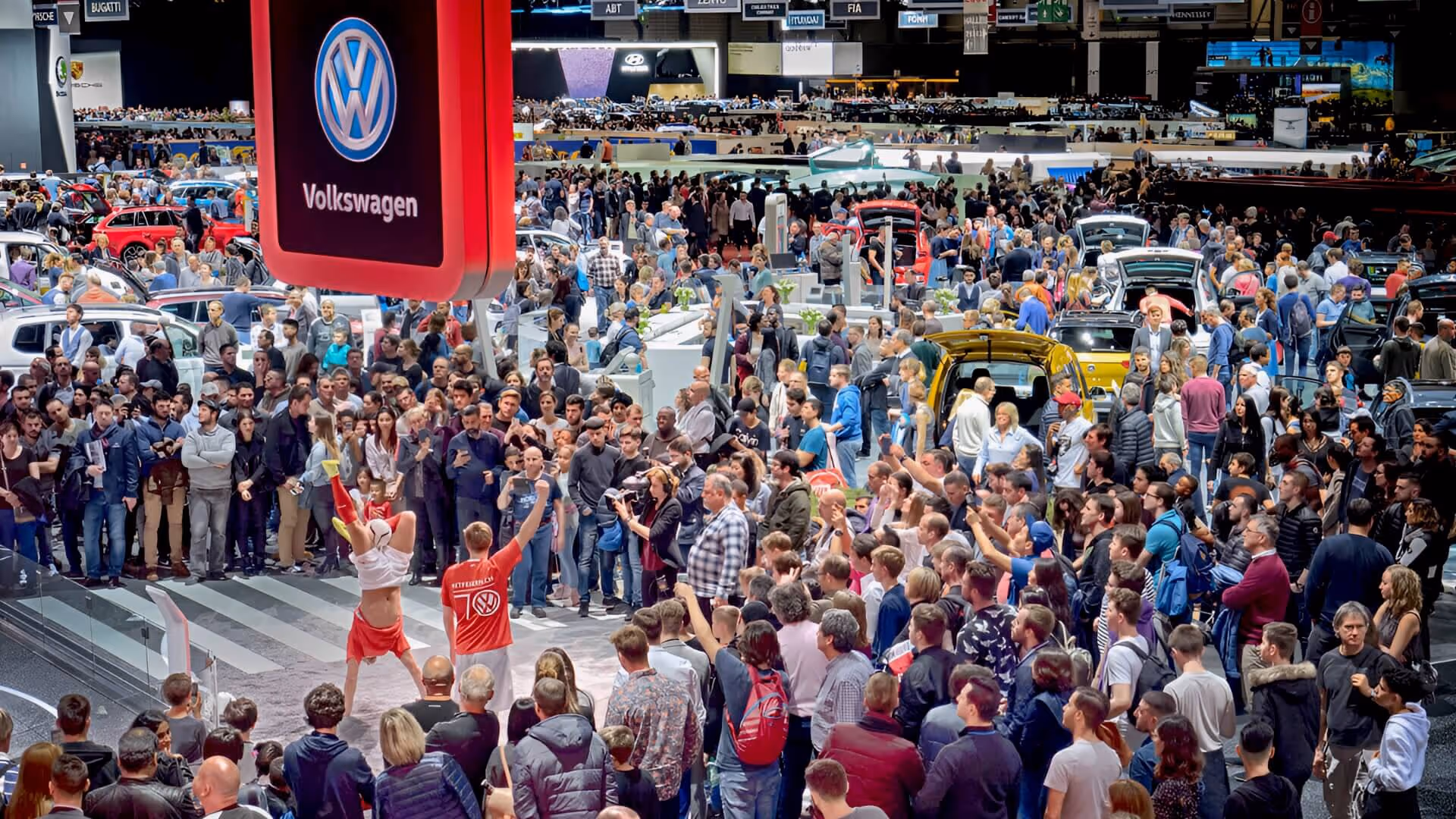Menschenmenge auf einer Messe, die eine Darbietung vor einem großen Volkswagen-Logo verfolgt.