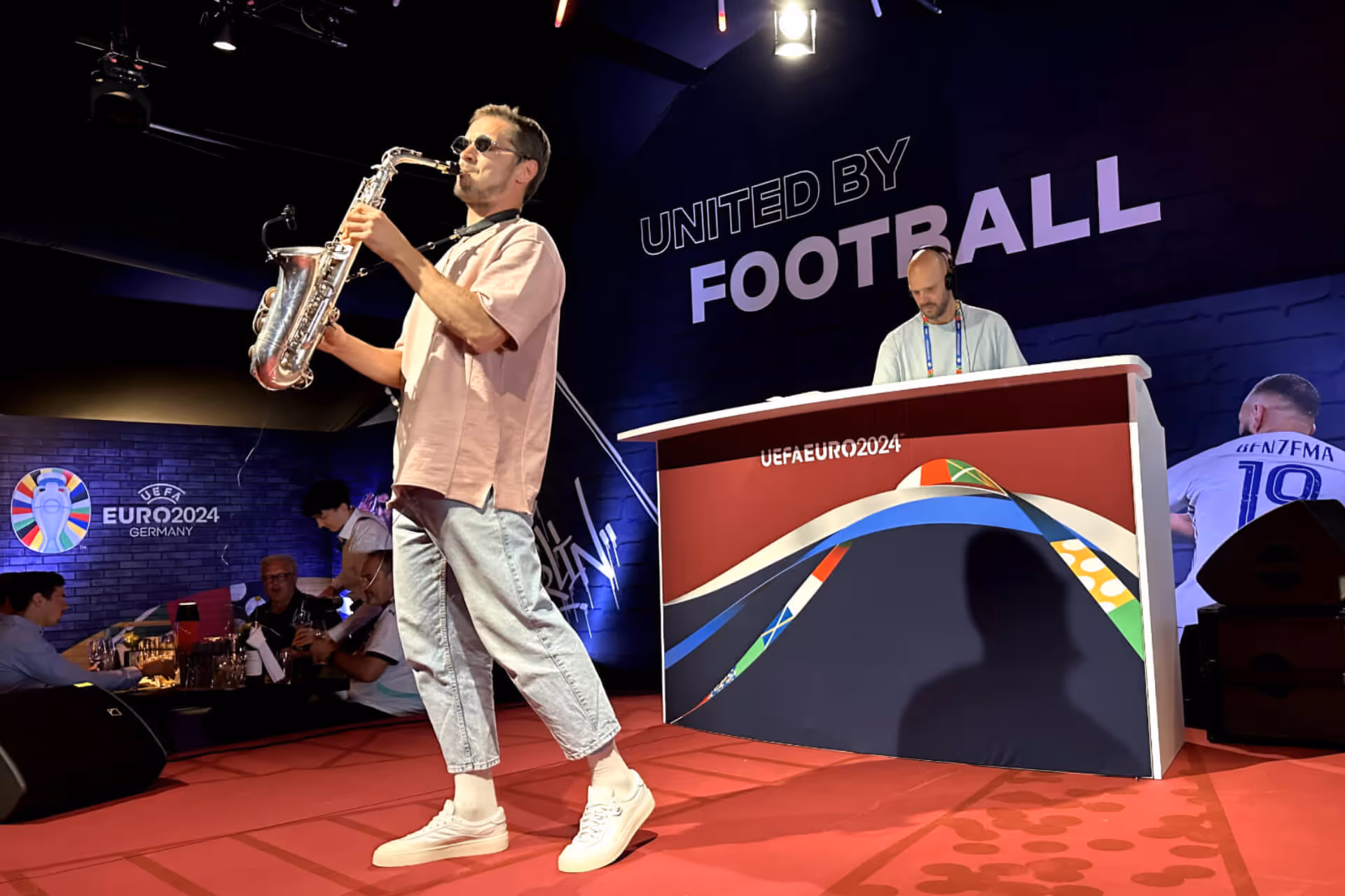Mann spielt Saxophon auf roter Bühne bei UEFA EURO 2024 Veranstaltung mit DJ und Zuschauern.