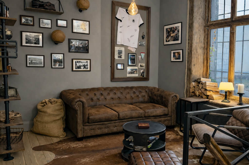 Gemütliche Ecke mit braunem Chesterfield-Sofa, Lederstuhl, runden Couchtisch und Wänden mit eingerahmten Fotos und einem signierten weißen Trikot.