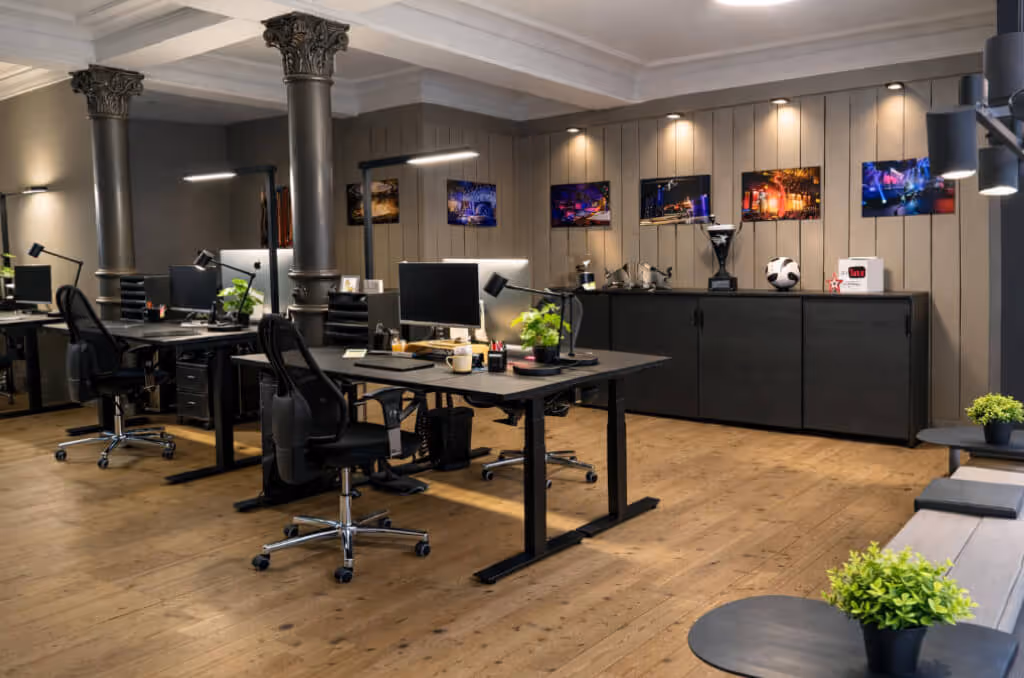 Modernes Büro mit schwarzen Schreibtischen, ergonomischen Stühlen und mehreren Pflanzen, Holzboden und dekorativen Säulen.