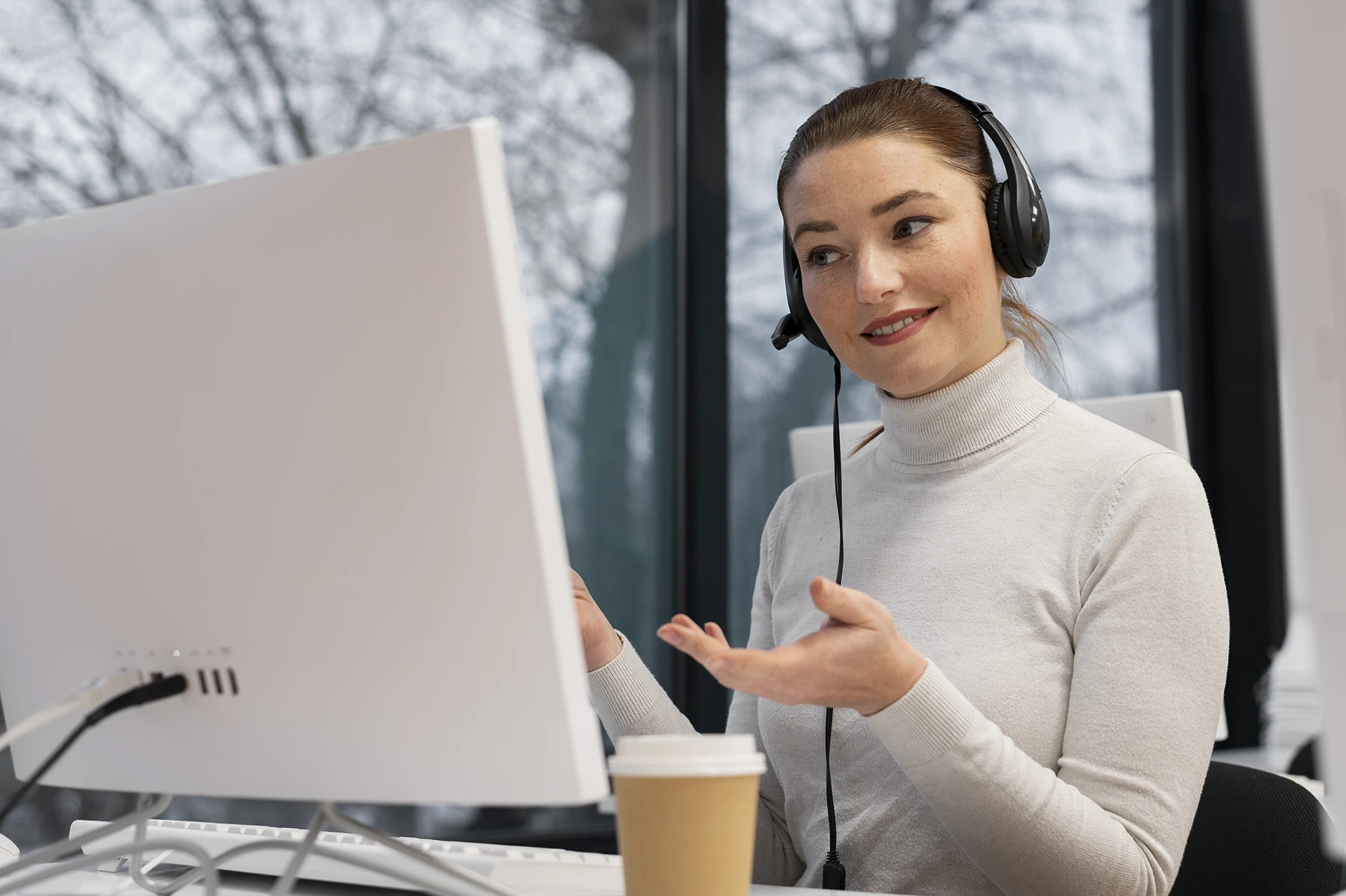 Vrouwelijke medewerker van ClikQ met headset die voor een computer zit en vriendelijk spreekt.