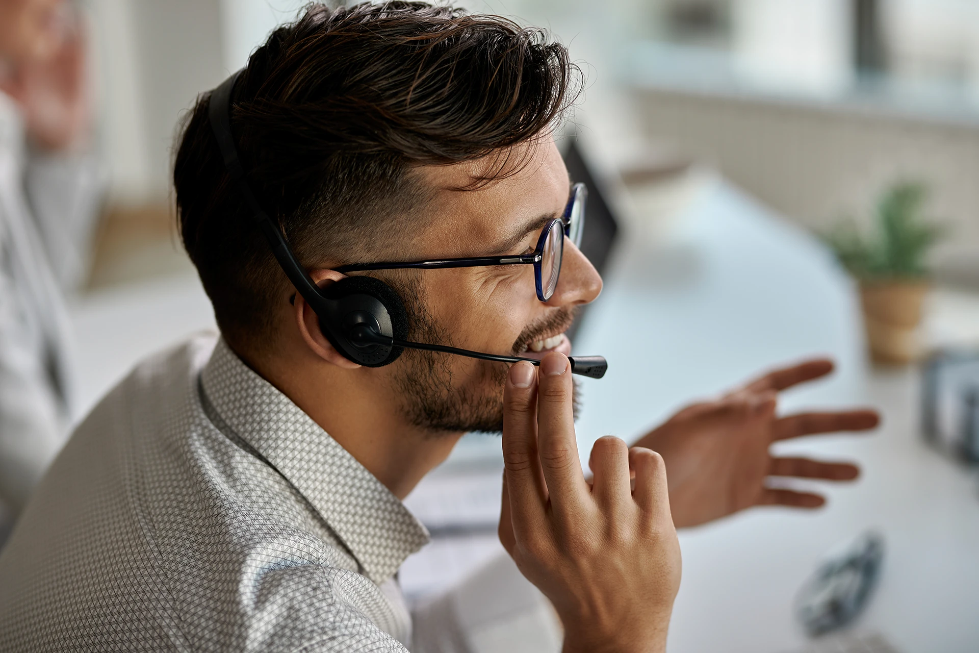 Mannelijke medewerker van ClikQ met bril en headset die glimlachend spreekt tijdens een videogesprek op kantoor.