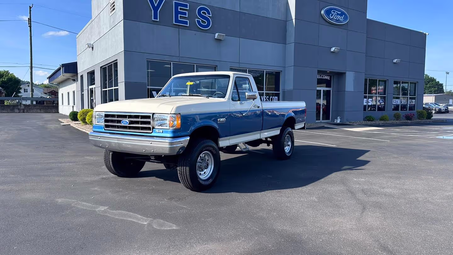 Vintage white and blue pickup truck parked in front of Yes Ford's dealership on a sunny day