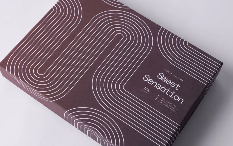 Dark chocolate bar packaging labeled Sweet Sensation with modern white line patterns on a brown background.