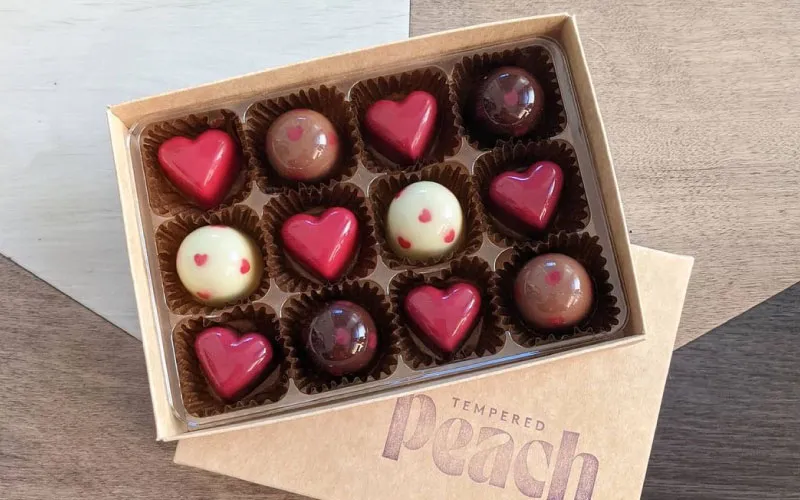 Box of assorted chocolates including red heart-shaped and round chocolates with heart decorations.
