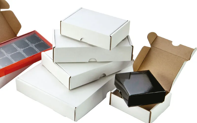 Stack of white cardboard boxes with one black box inside an open brown box and a red box with a window on the side.