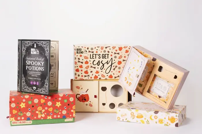 Three decorative tea gift boxes with seasonal designs and themes, including a spooky potions book and a cozy autumn box.