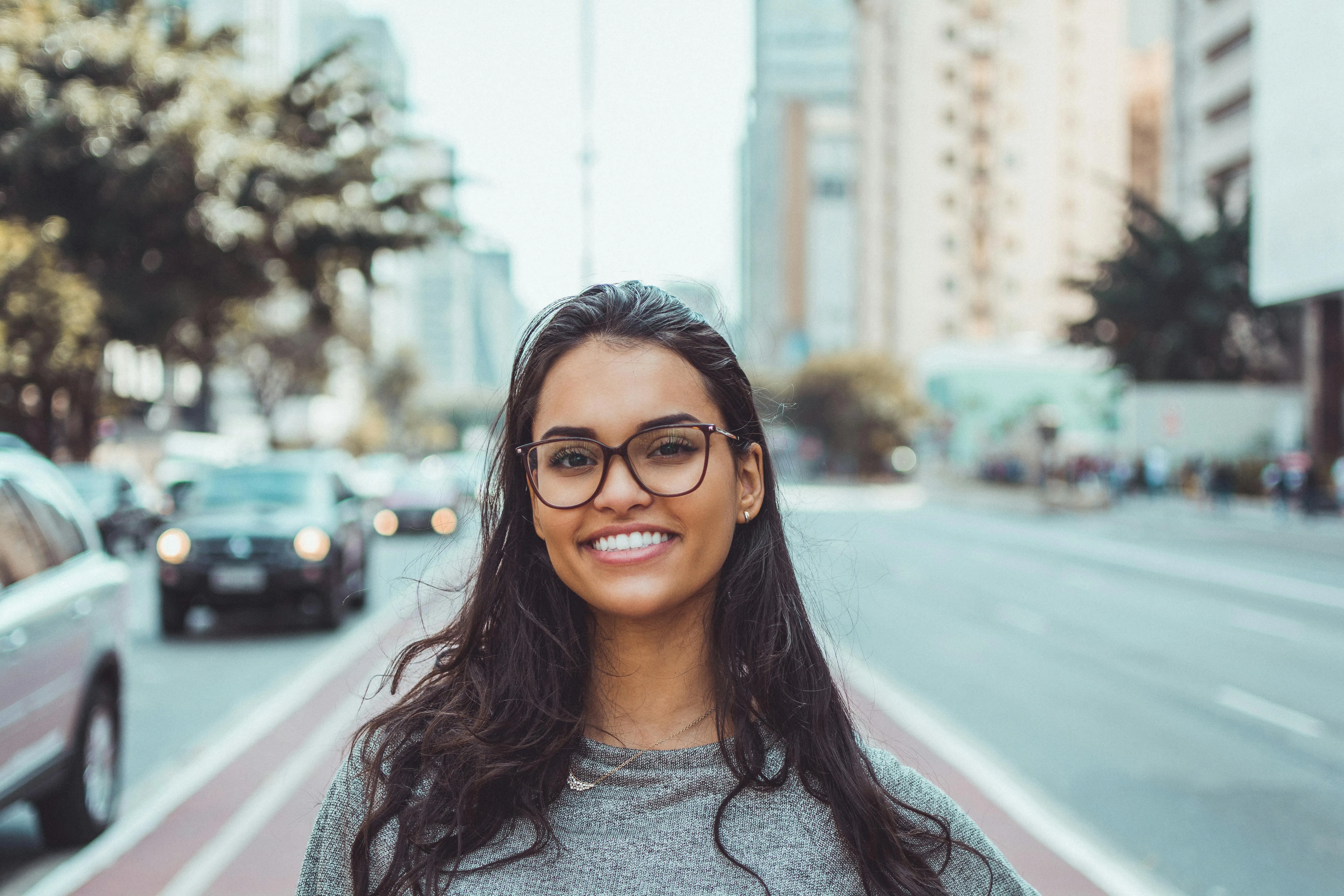 Smiling person with glasses standing on city street with blurred background