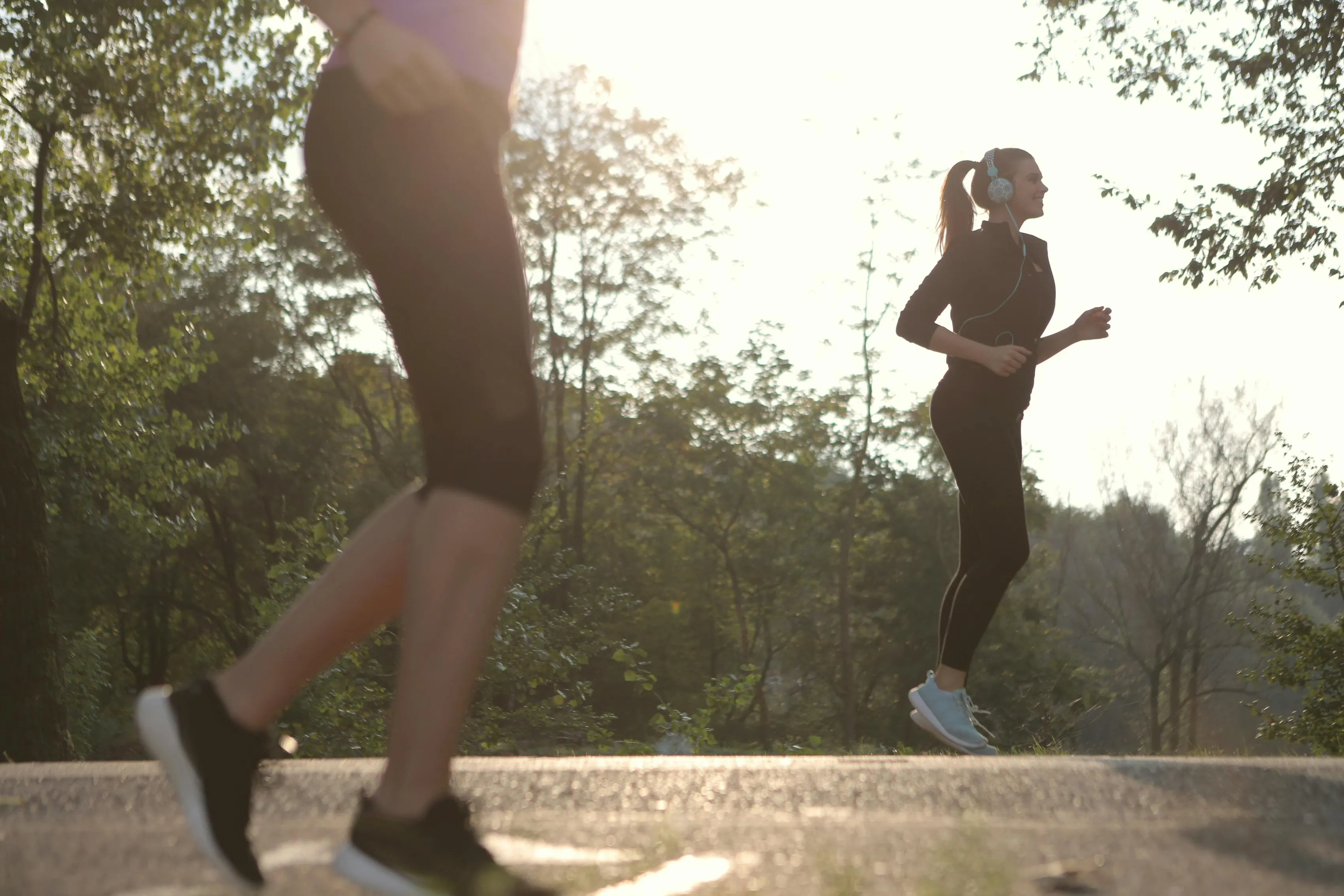 Two runners with headphones exercising on outdoor path at sunrise