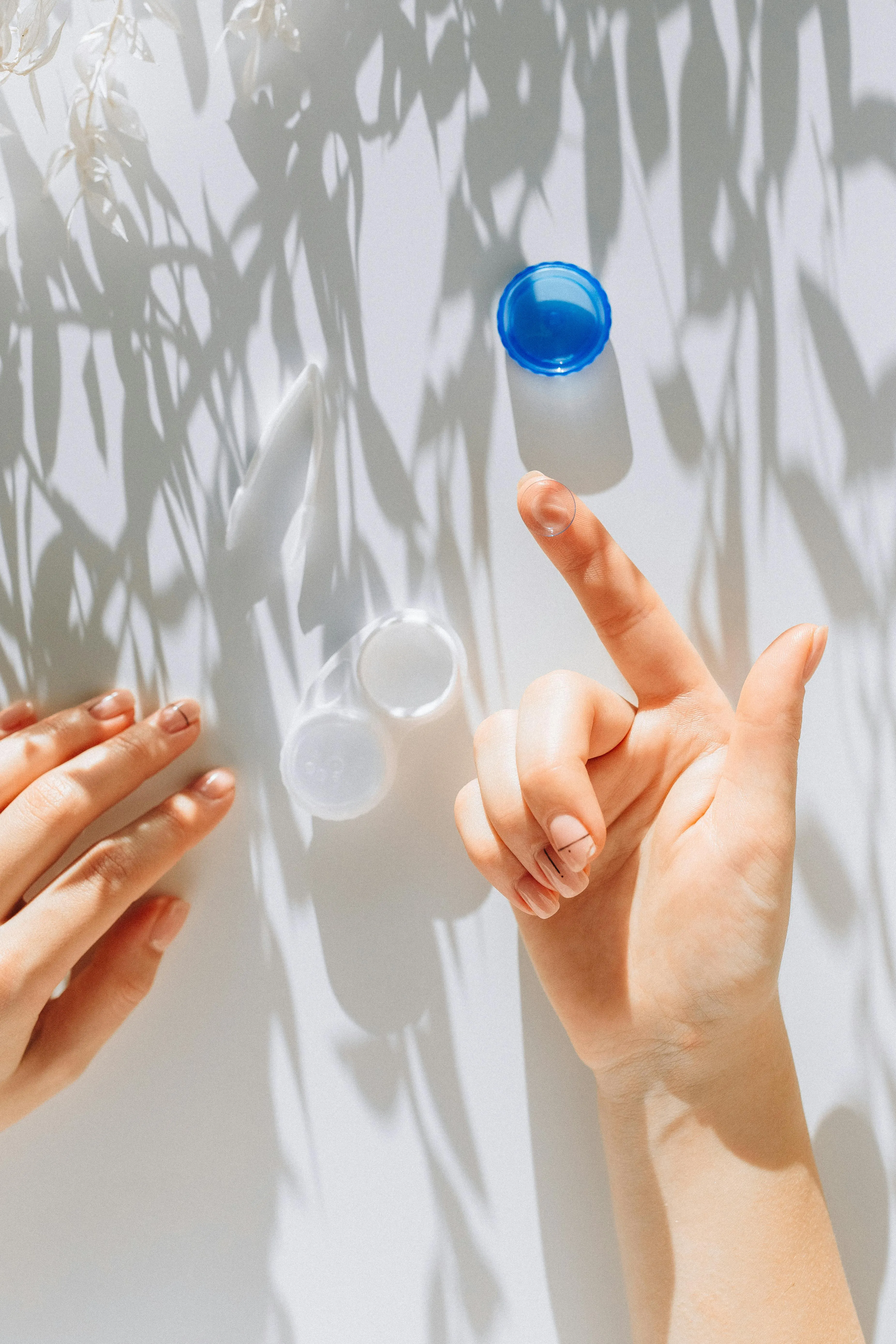 Hands reaching towards blue and clear glass spheres with leaf shadows