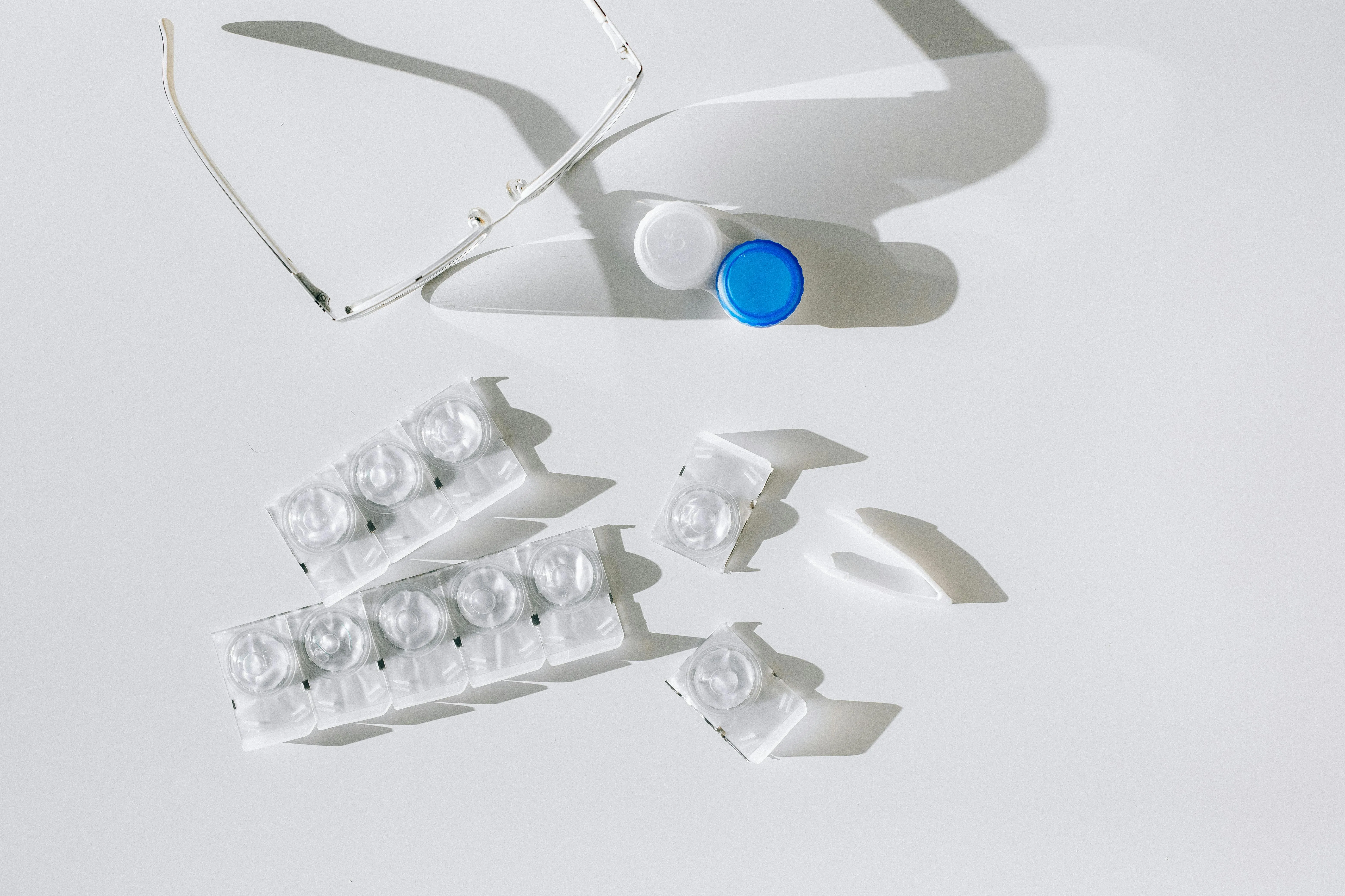 Eyeglasses, contact lens case, and blister packs on a white background