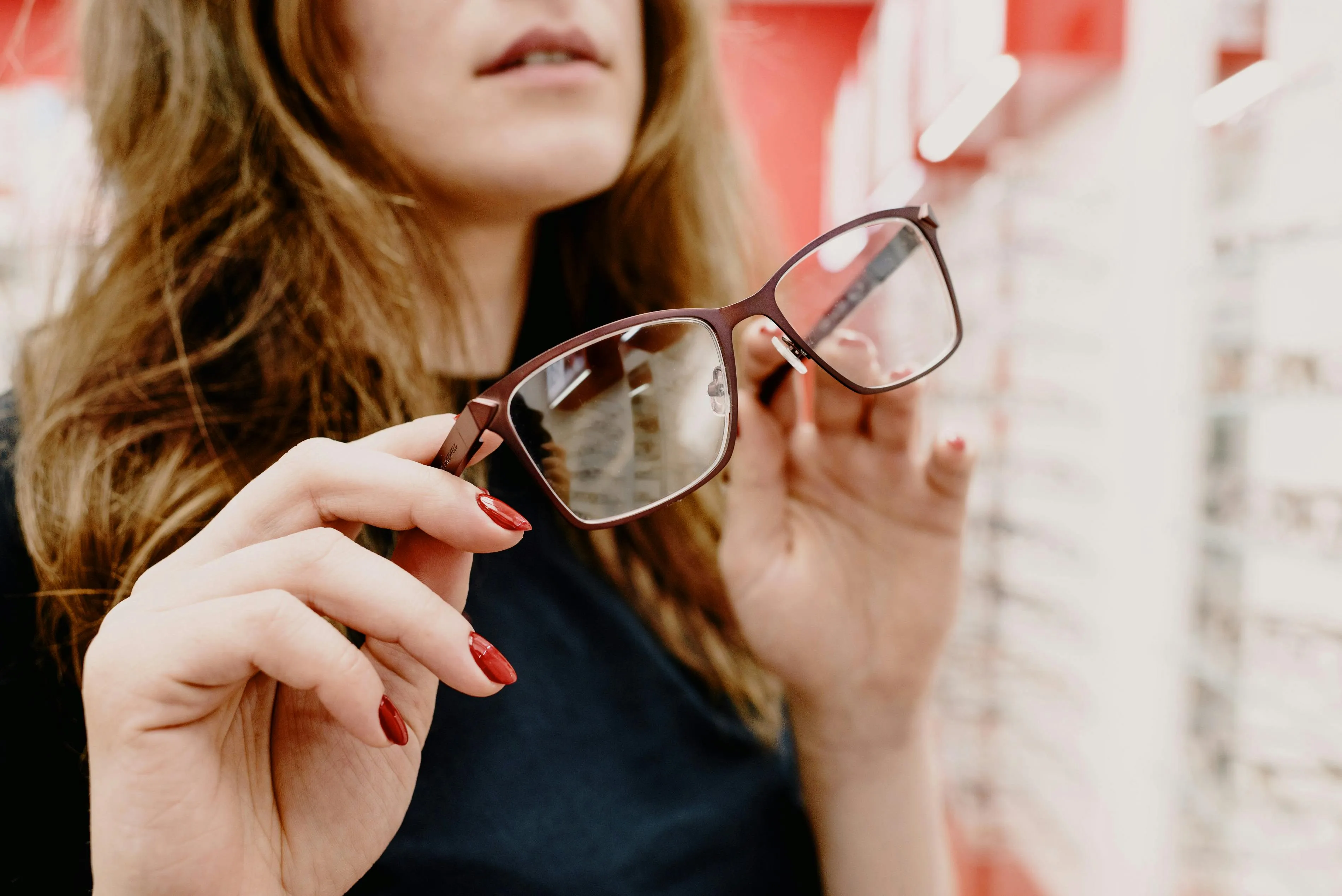 Person trying on brown glasses with red nail polish in optical store
