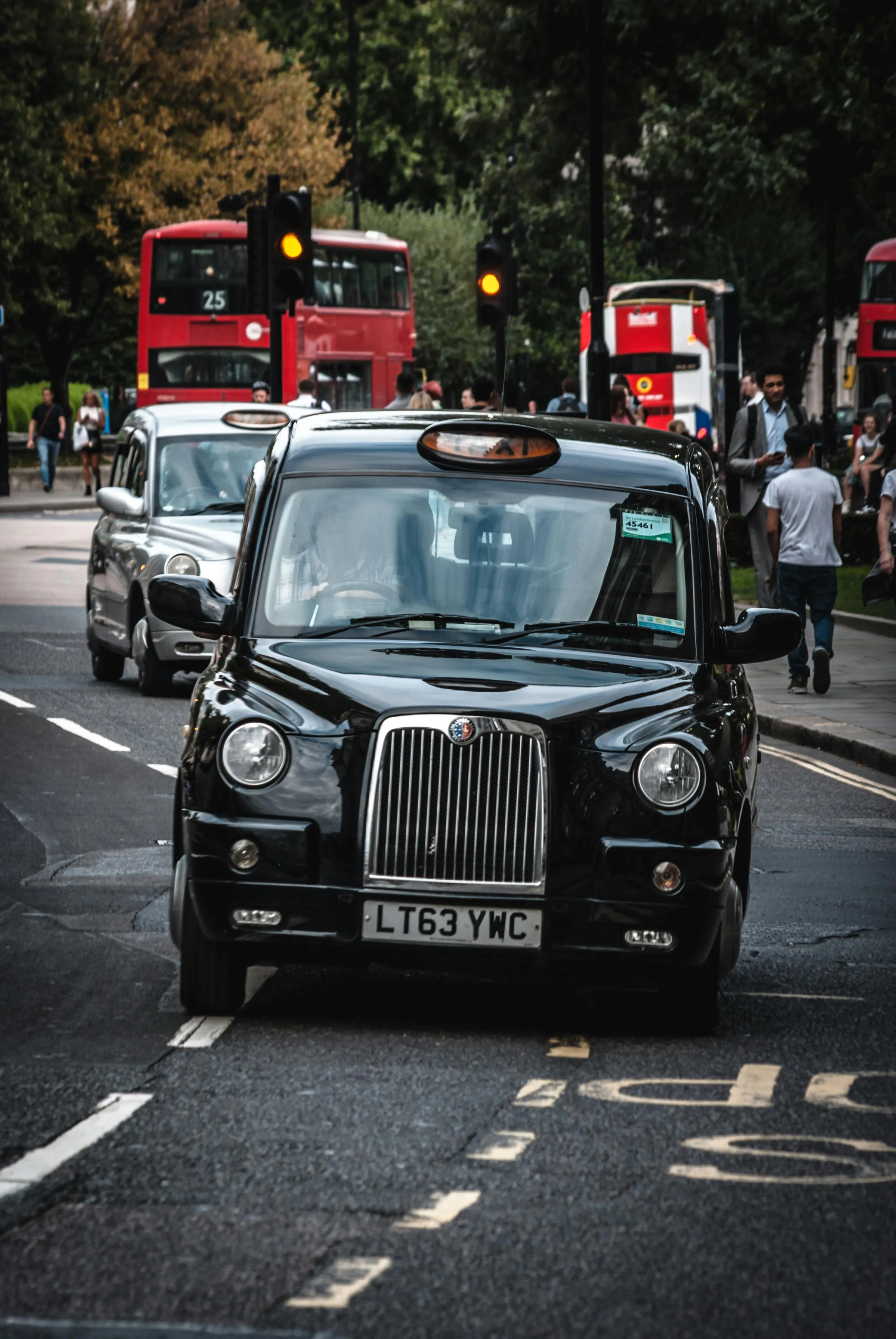 Black London taxi on busy street with red double-decker buses in background