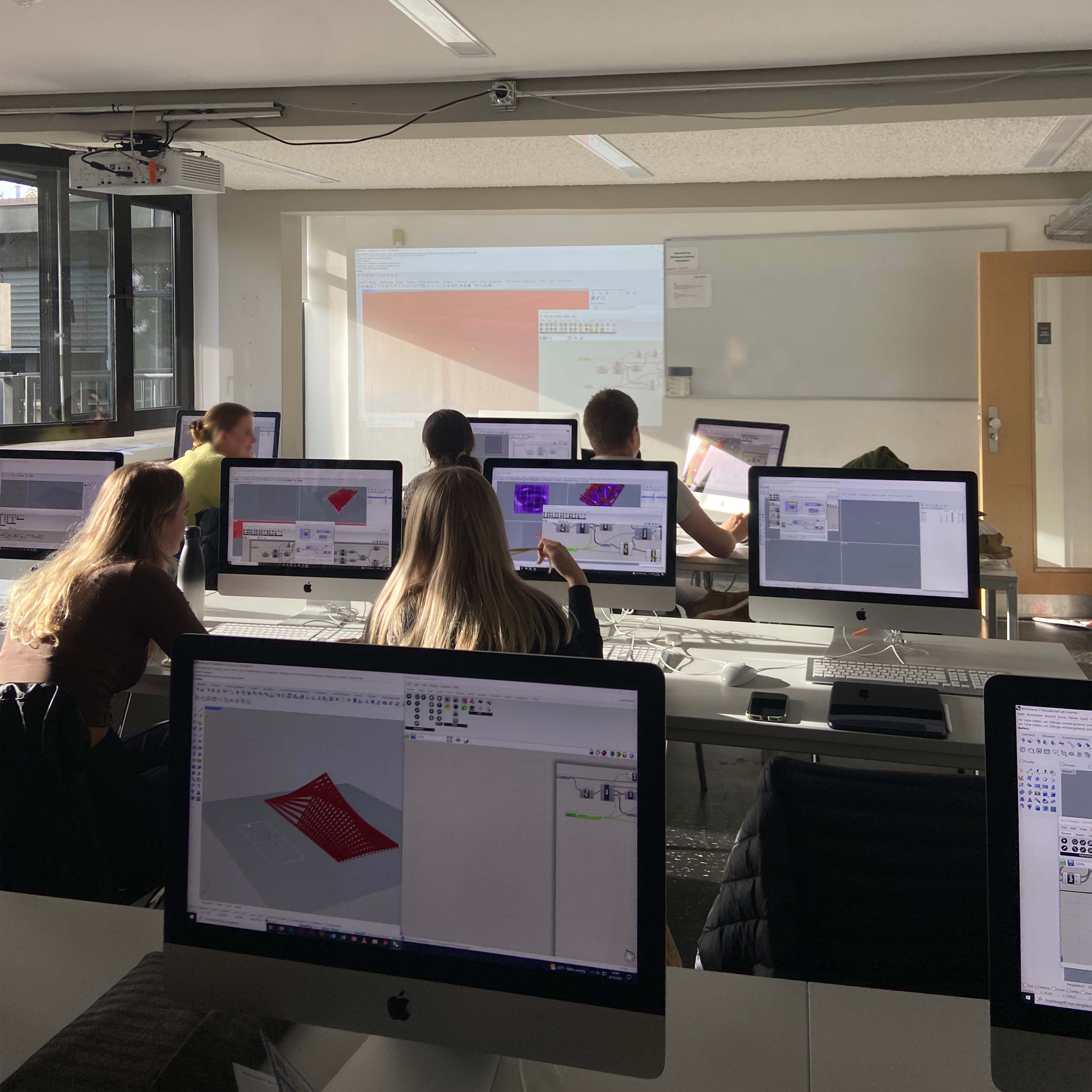 studio morfin- dozententätigkeit. Studierende arbeiten an Computern mit 3D-Modellierungssoftware in einem hellen Computerraum mit Projektor.