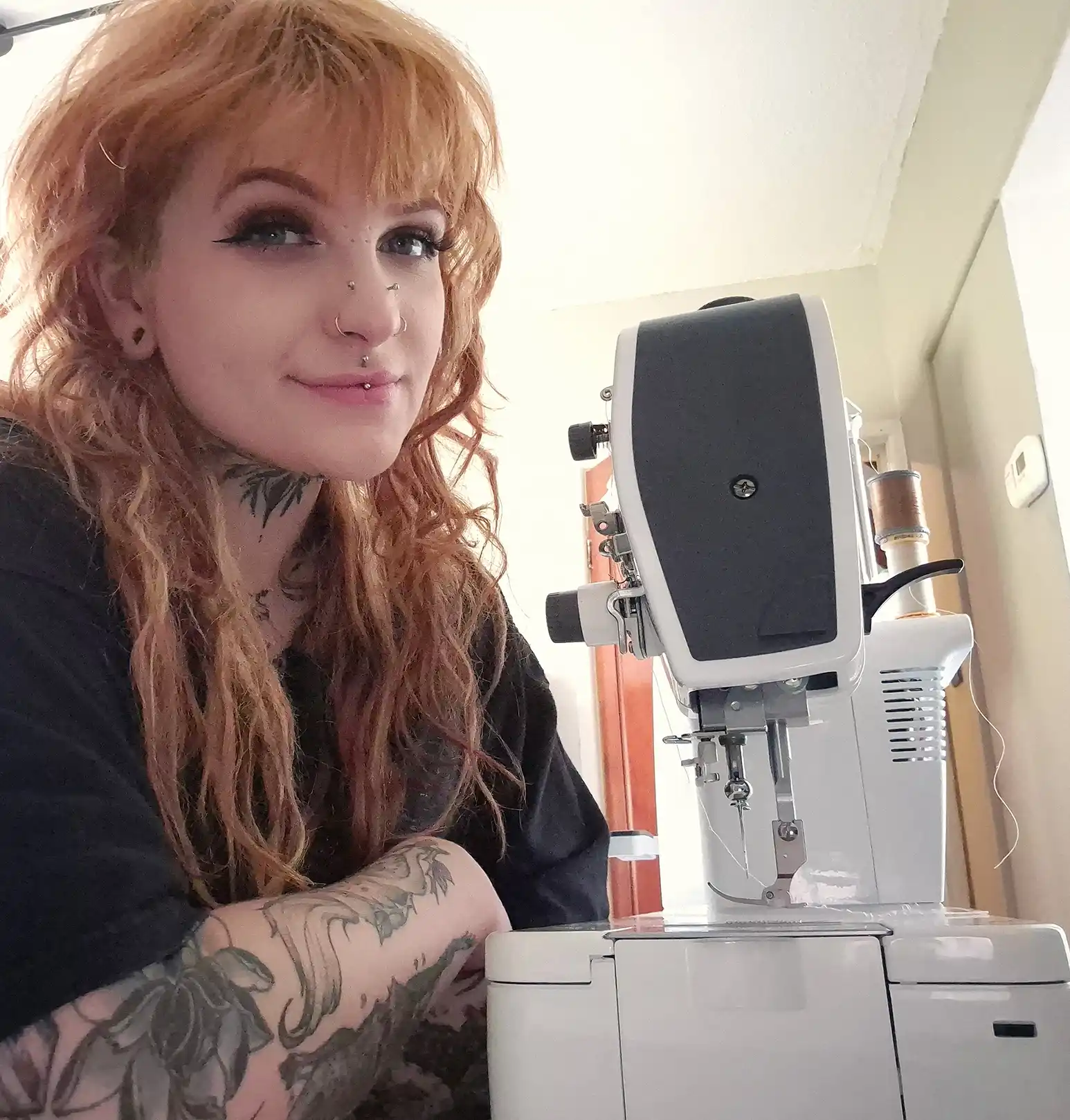 Jodie Cooper Jodie smiling sitting beside her sewing machine in her workspace.