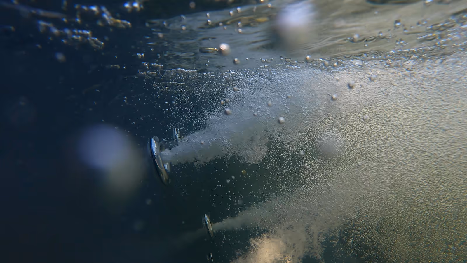 Underwater view of multiple jets releasing streams of bubbles into dark water.