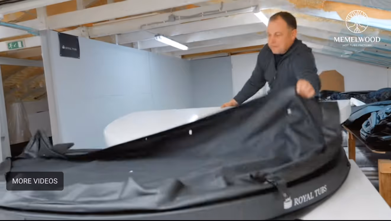 A man adjusting a black cover on a Royal Tubs hot tub inside a workshop.