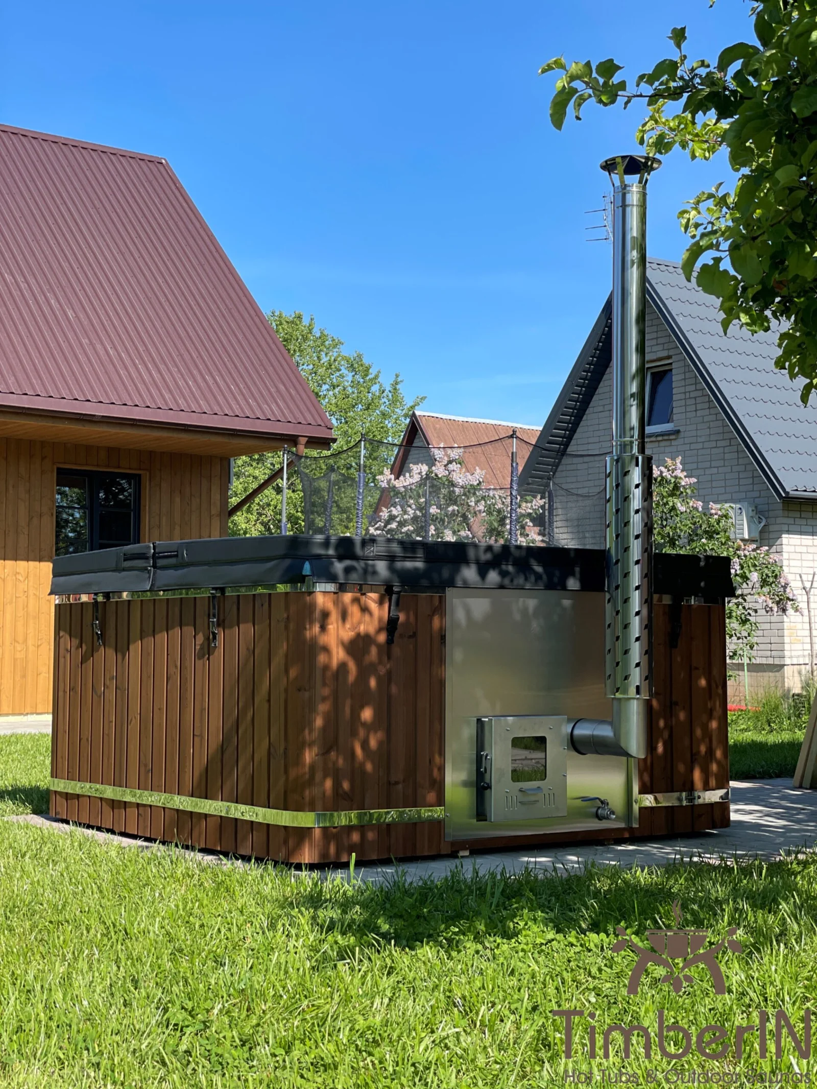 Round wooden hot tub with white interior and a tall metal chimney pipe.