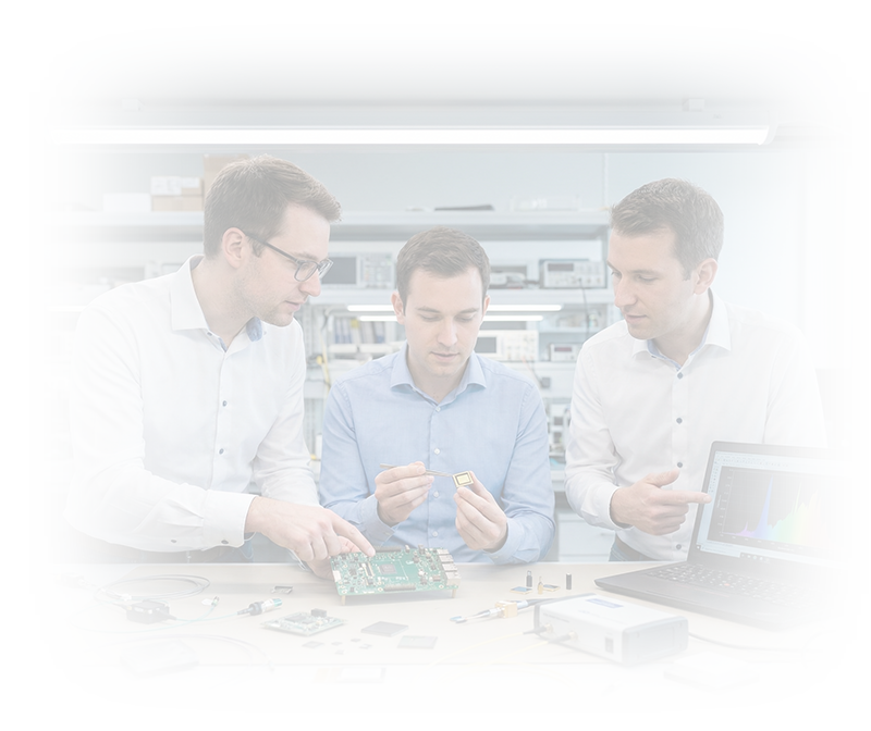 Three engineers in a lab analyzing a circuit board and a microchip with technical equipment and a laptop displaying a colorful graph.