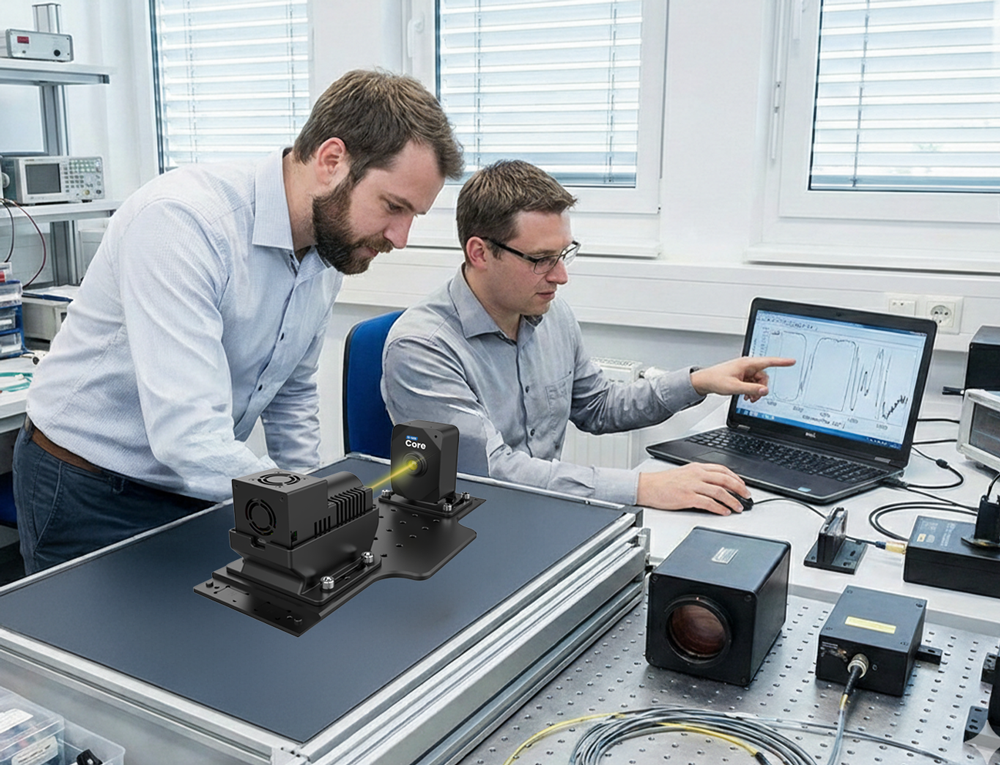 Two men working in a laboratory with a laptop displaying scientific graphs and a mounted laser system on an optical table.