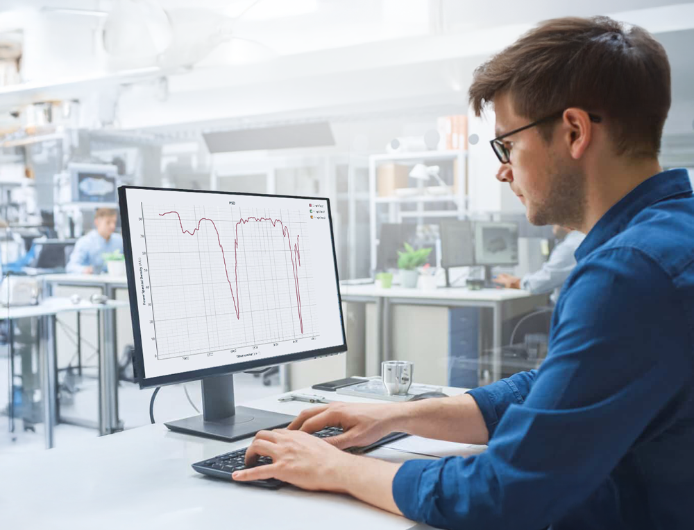 Man in glasses working on a computer in a lab, analyzing a graph displayed on the monitor.