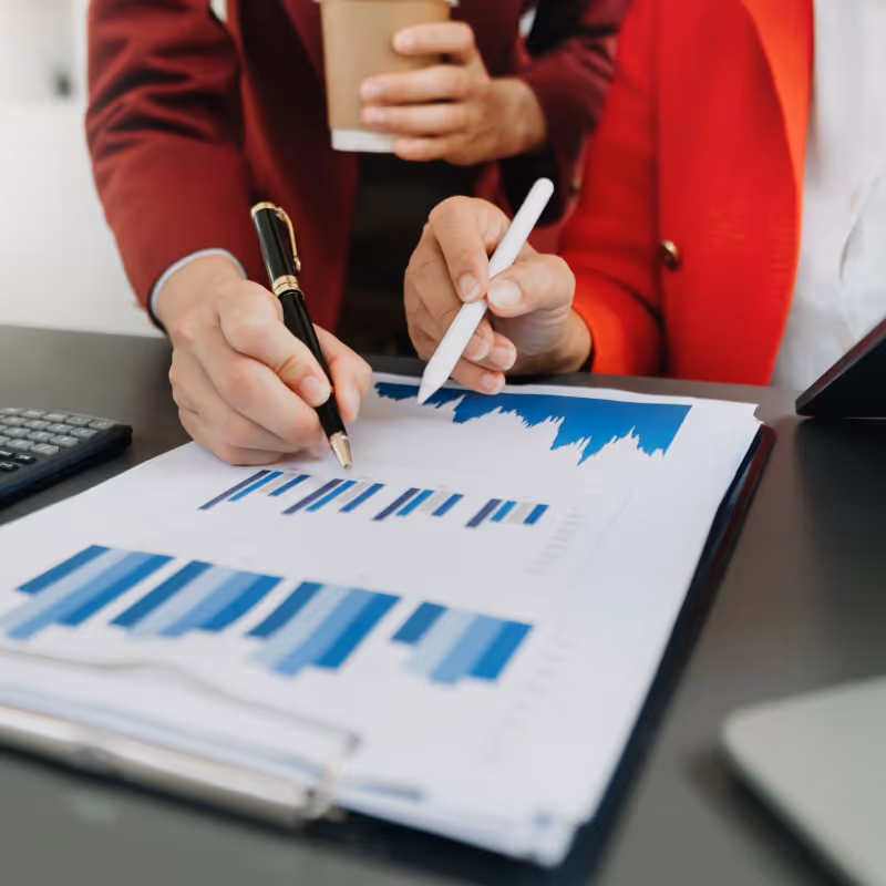 Deux personnes analysant des graphiques financiers sur papier avec un stylo et un crayon.