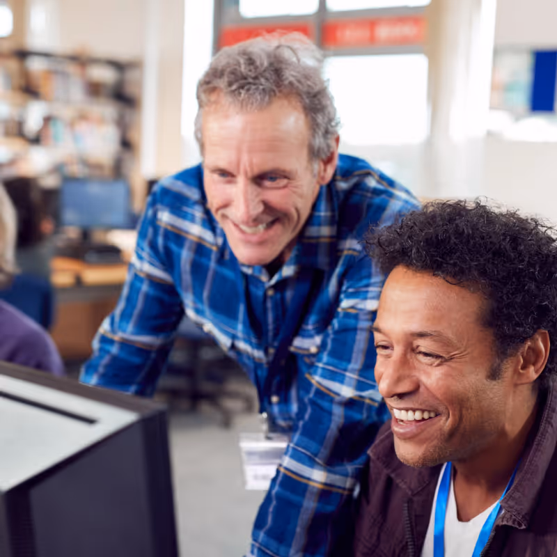 Deux hommes souriants regardant un écran d'ordinateur dans un bureau lumineux.