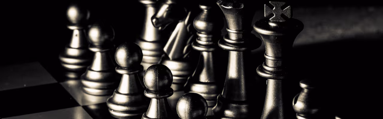 Pièces d'échecs métalliques sur un plateau en lumière basse, avec le roi et la reine visibles.