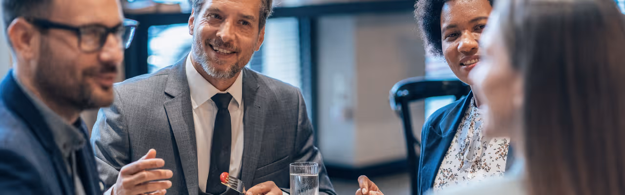 Quatre personnes en tenue professionnelle discutent en mangeant lors d'un repas d'affaires.