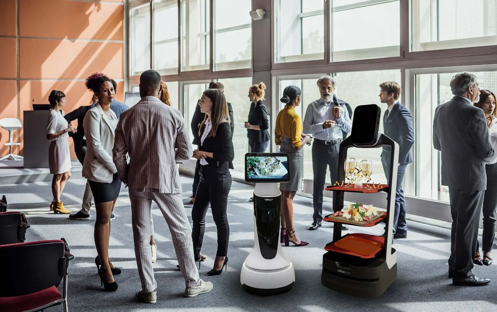 Des professionnels en tenue d'affaires discutent près de robots de service dans une salle lumineuse.