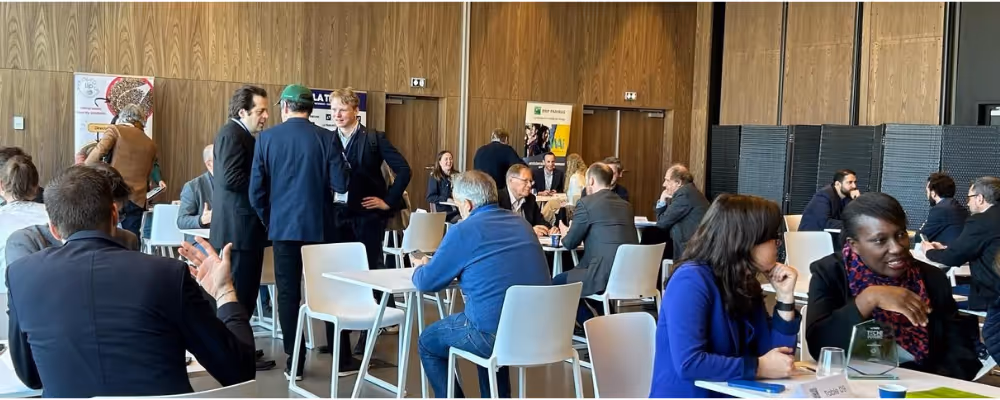 Personnes en tenue professionnelle discutant autour de tables blanches dans une salle en bois.