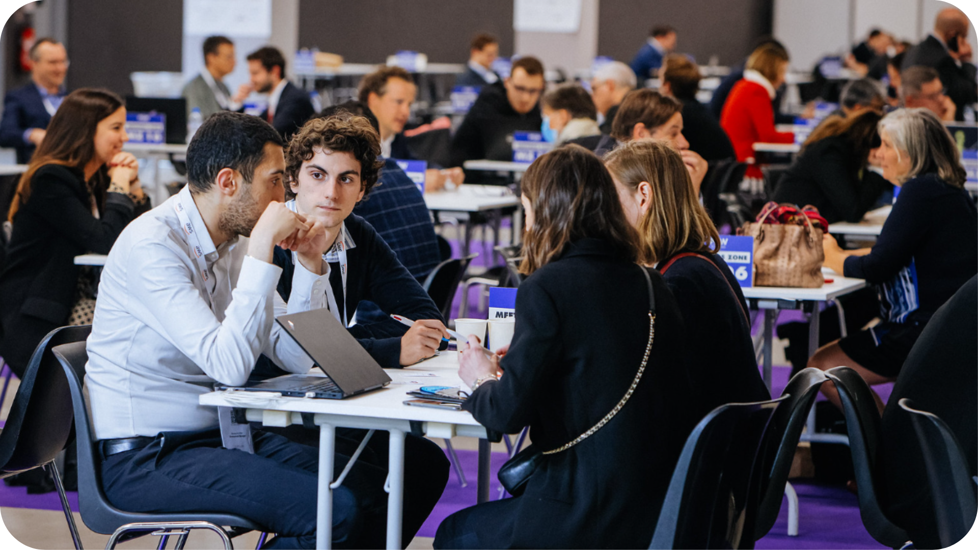 Groupe de personnes discutant autour d'une table lors d'un événement professionnel en salle.