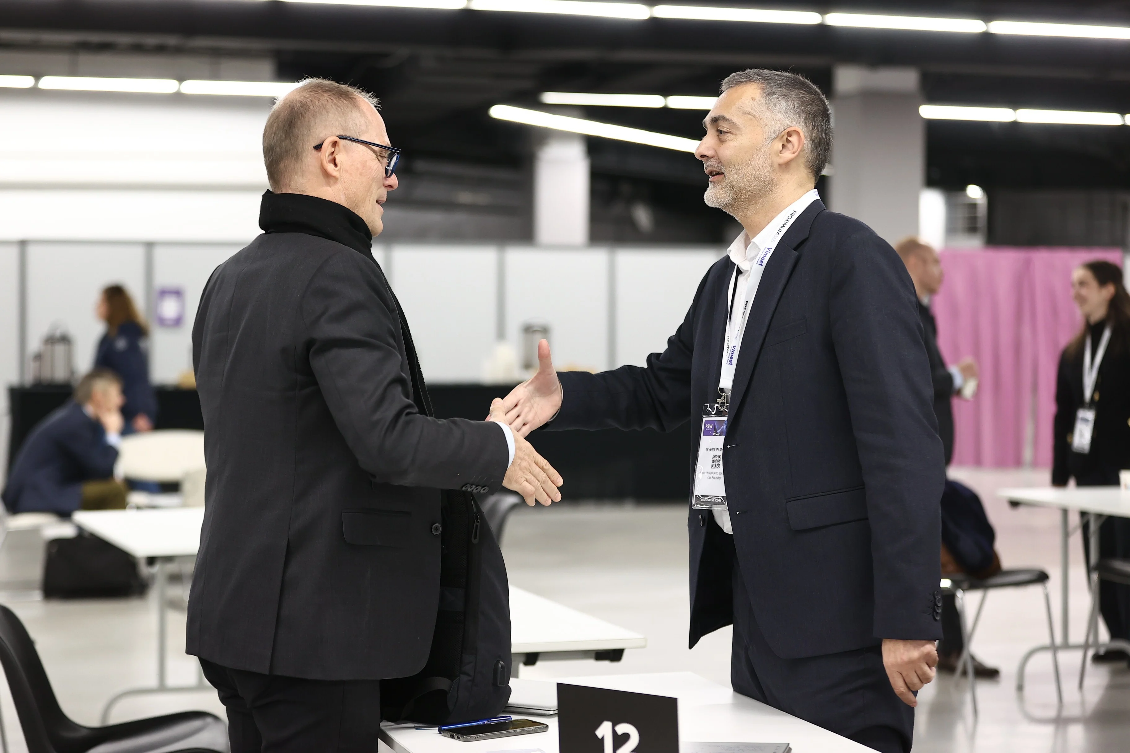 Deux hommes en costume se serrant la main lors d'une rencontre professionnelle en salle de conférence.