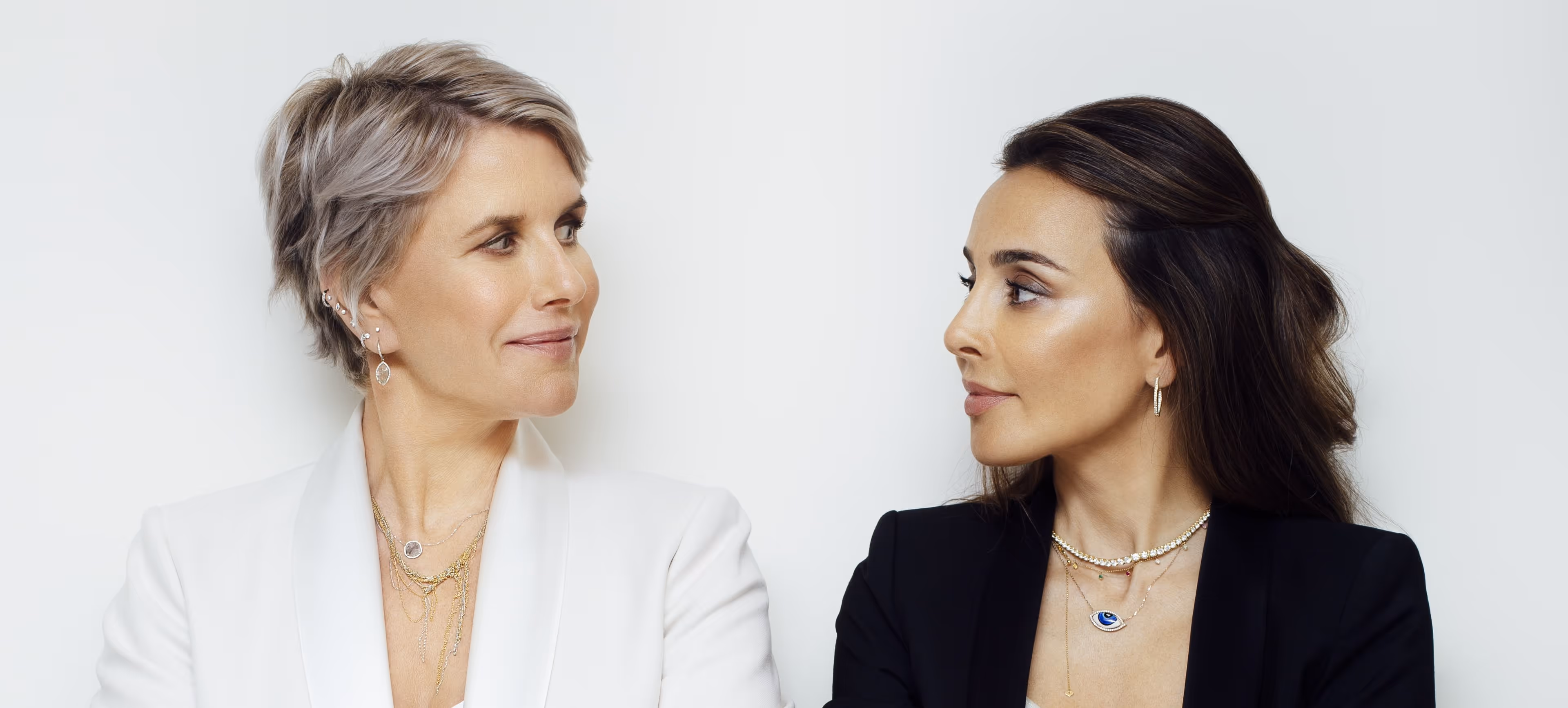 Two women in blazers facing each other with confident expressions against a plain white background.