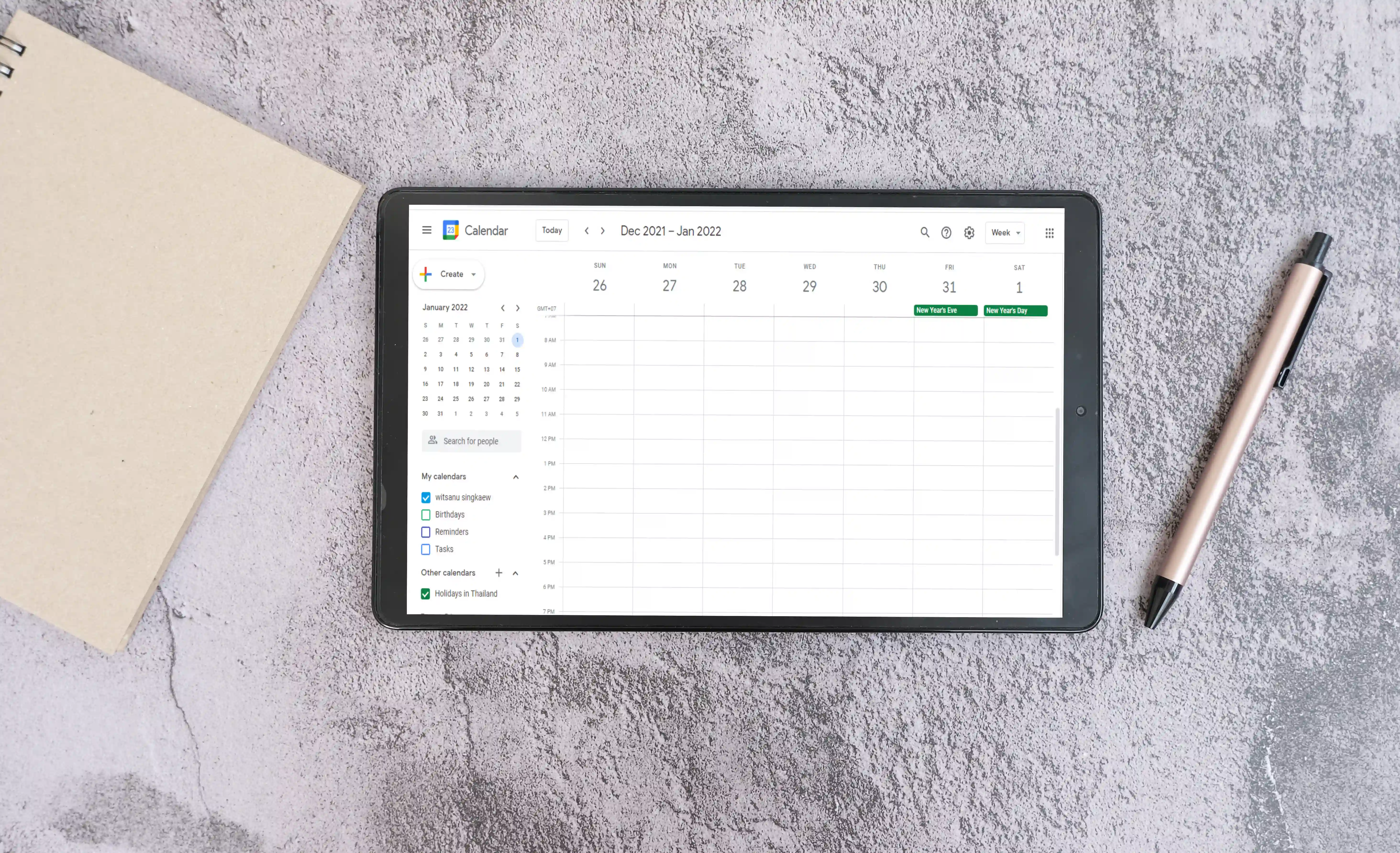 Tablet ligger på et bord og viser en åben kalenderoversigt i Google Kalender. Ved siden af ligger en kuglepen og en notesblok. Billedet illustrerer planlægning og tidsstyring – en vigtig del af effektiv Telefonpasning, hvor aftaler og opkald skal koordineres præcist.