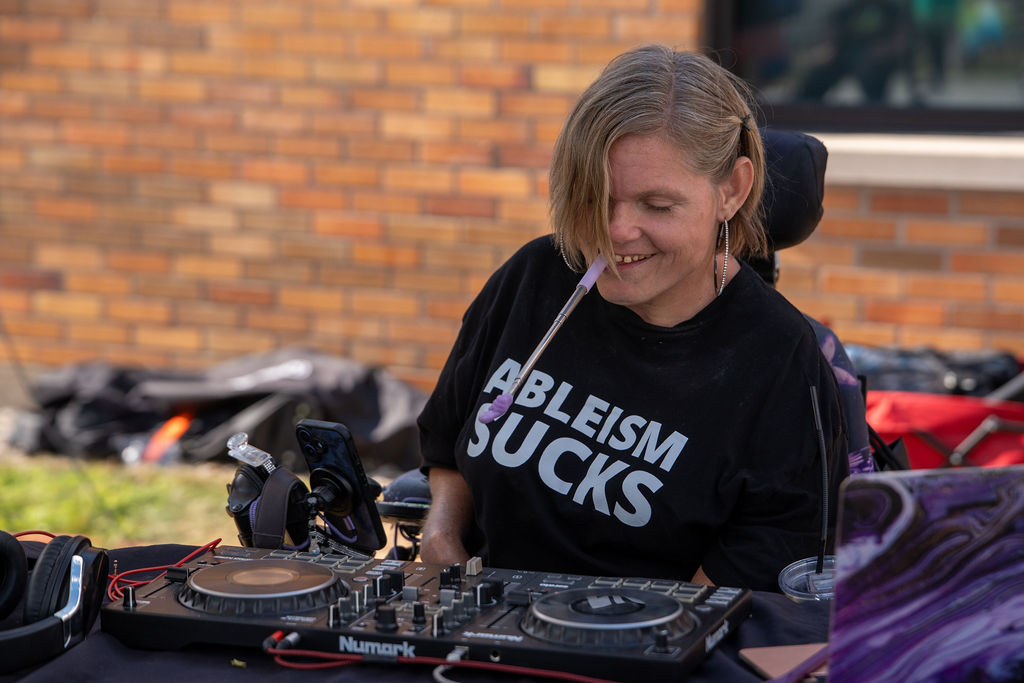 DJ Short-e With her turntable. She is wearing a black shirt with white text that reads Ableism Sucks