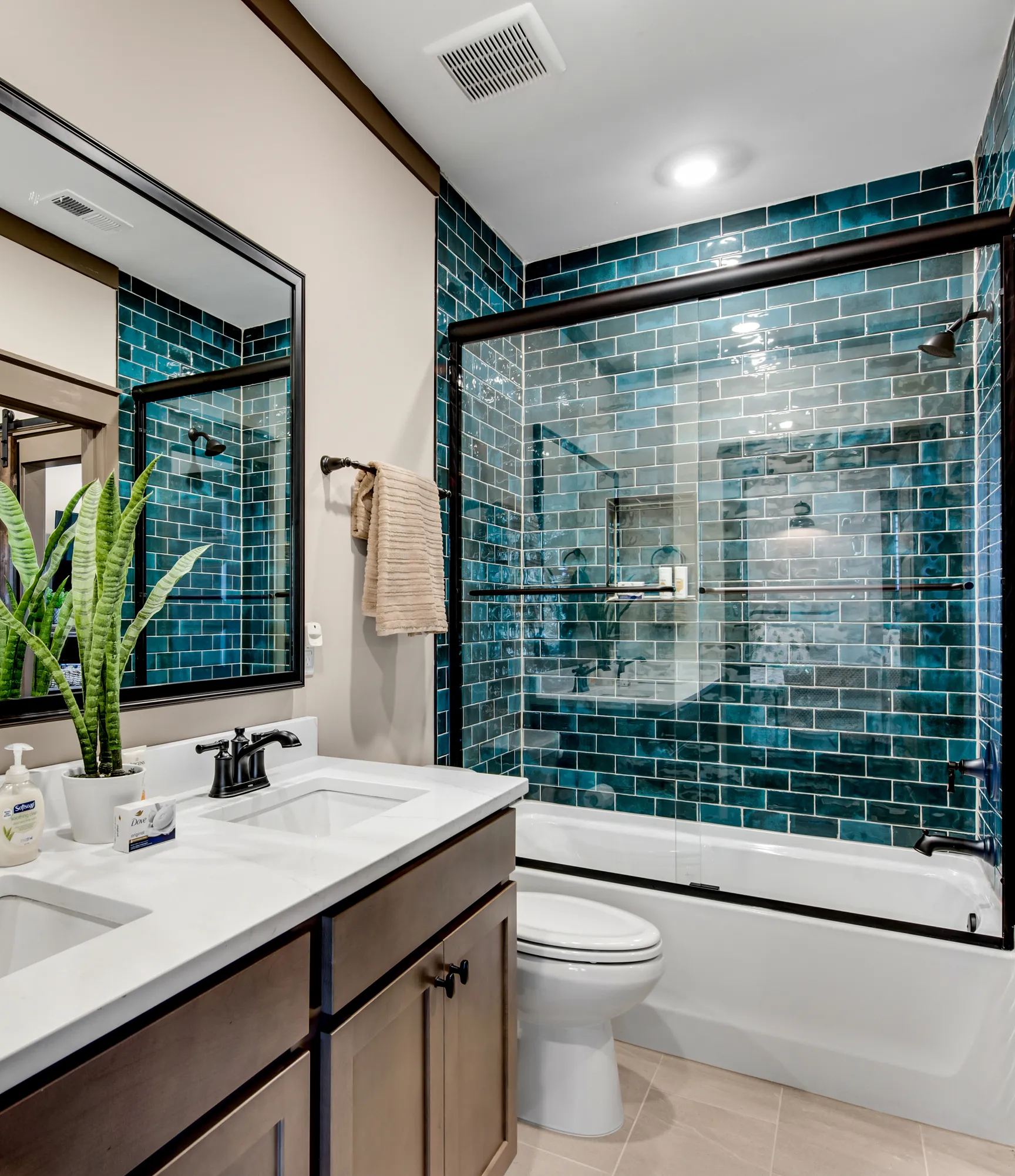 Stylish modern bathroom remodel featuring a double vanity with quartz countertop, rich wood cabinetry, and a bathtub with striking teal subway tile surround and glass enclosure showcasing quality renovation and elegant design.