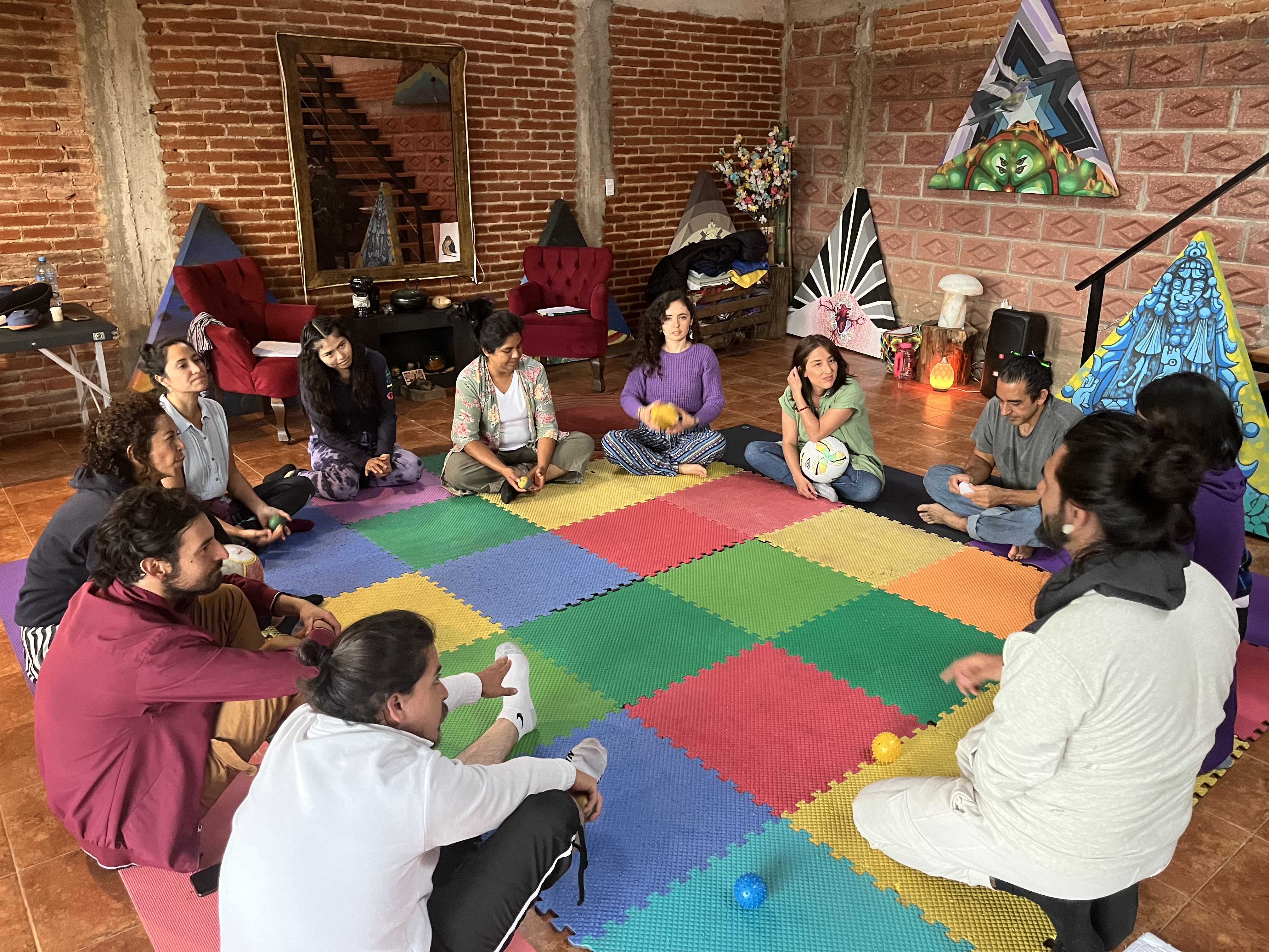 A circle of people gathered on the floor of a brick studio