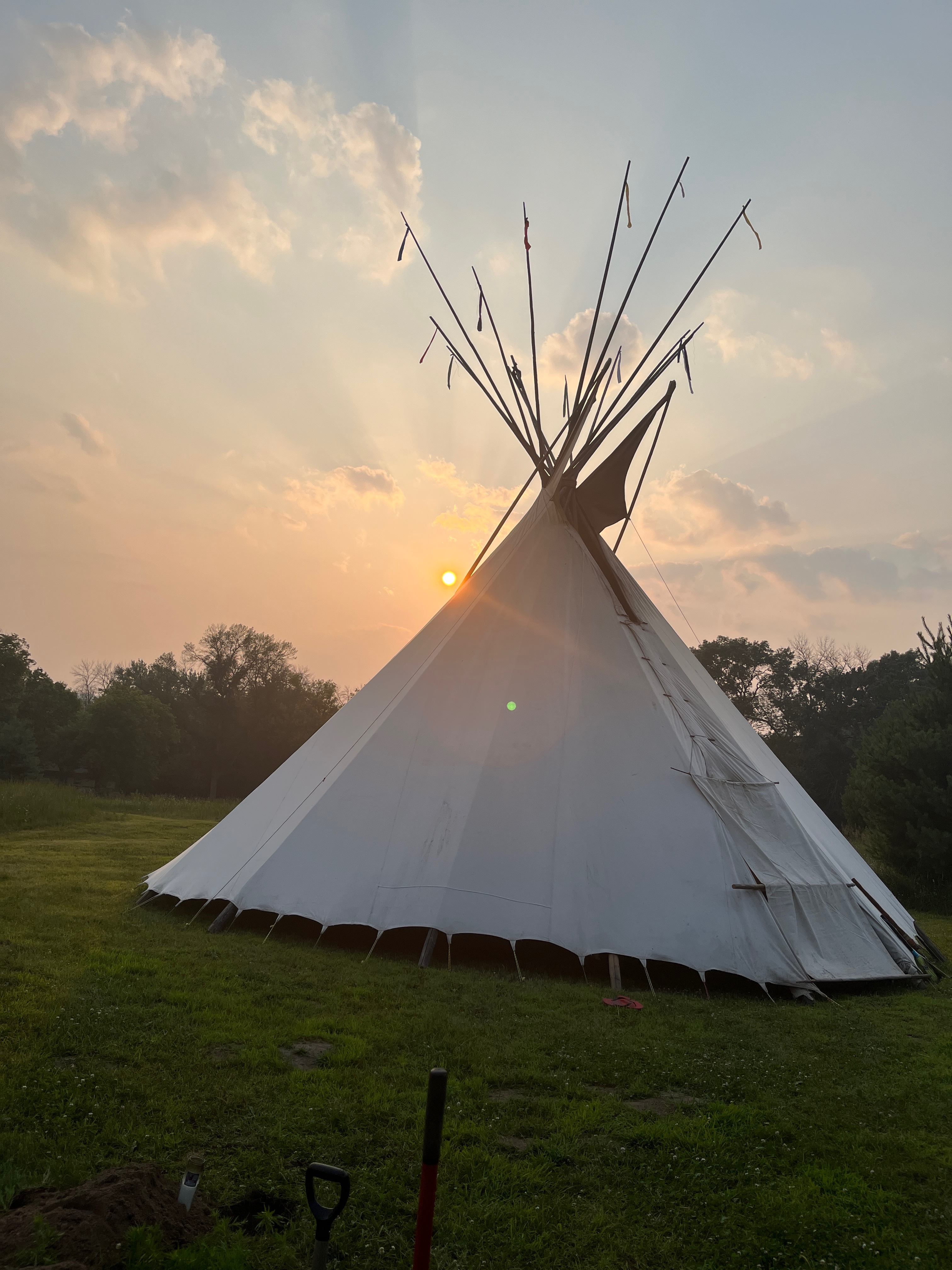 A white tipi in a meadow at sunset