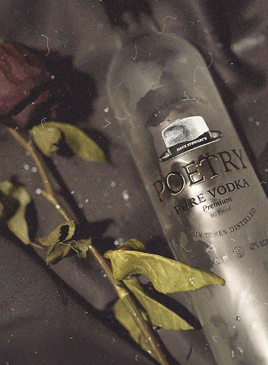 Bottle of Poetry Pure Vodka lying beside a green leafy branch on a dark surface.