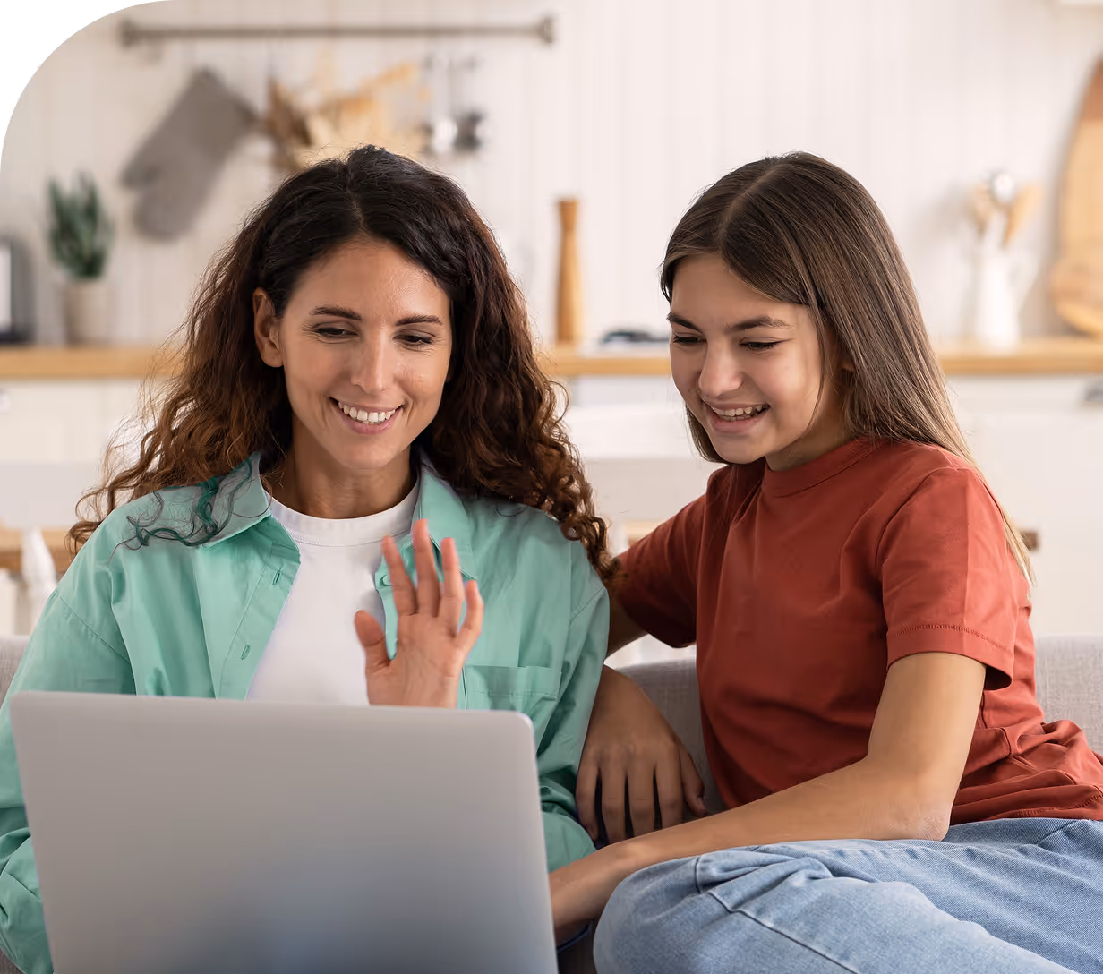 Mother and daughter smiling and waving during a video call at home.