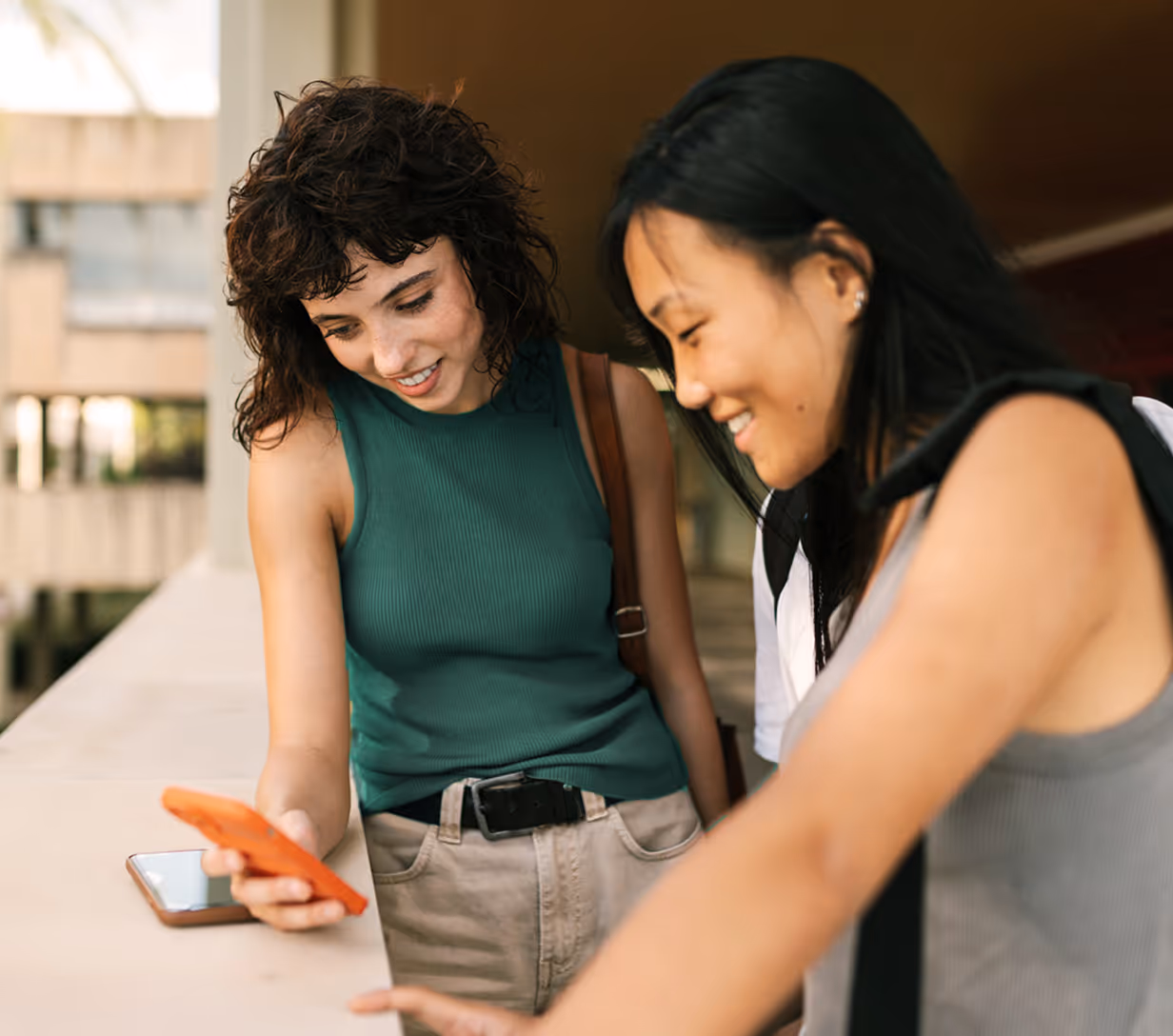 Two young adults looking at the phone while smiling.